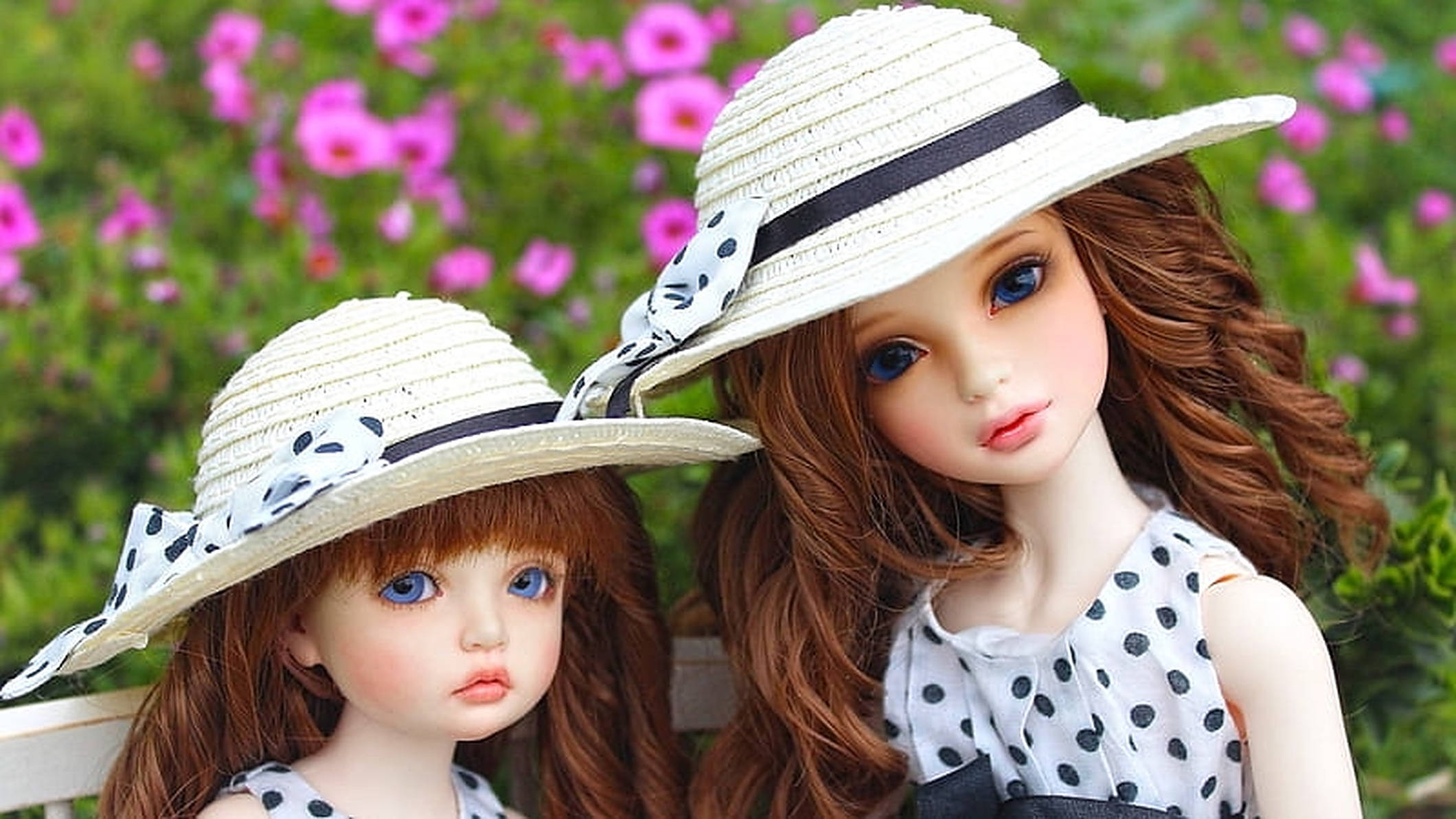 Doll 桌布 壁紙 — 兩個精緻的洋娃娃，藍眼睛、棕色頭髮，戴著相配的草帽和波點服裝，背景是粉紅色的花朵。
