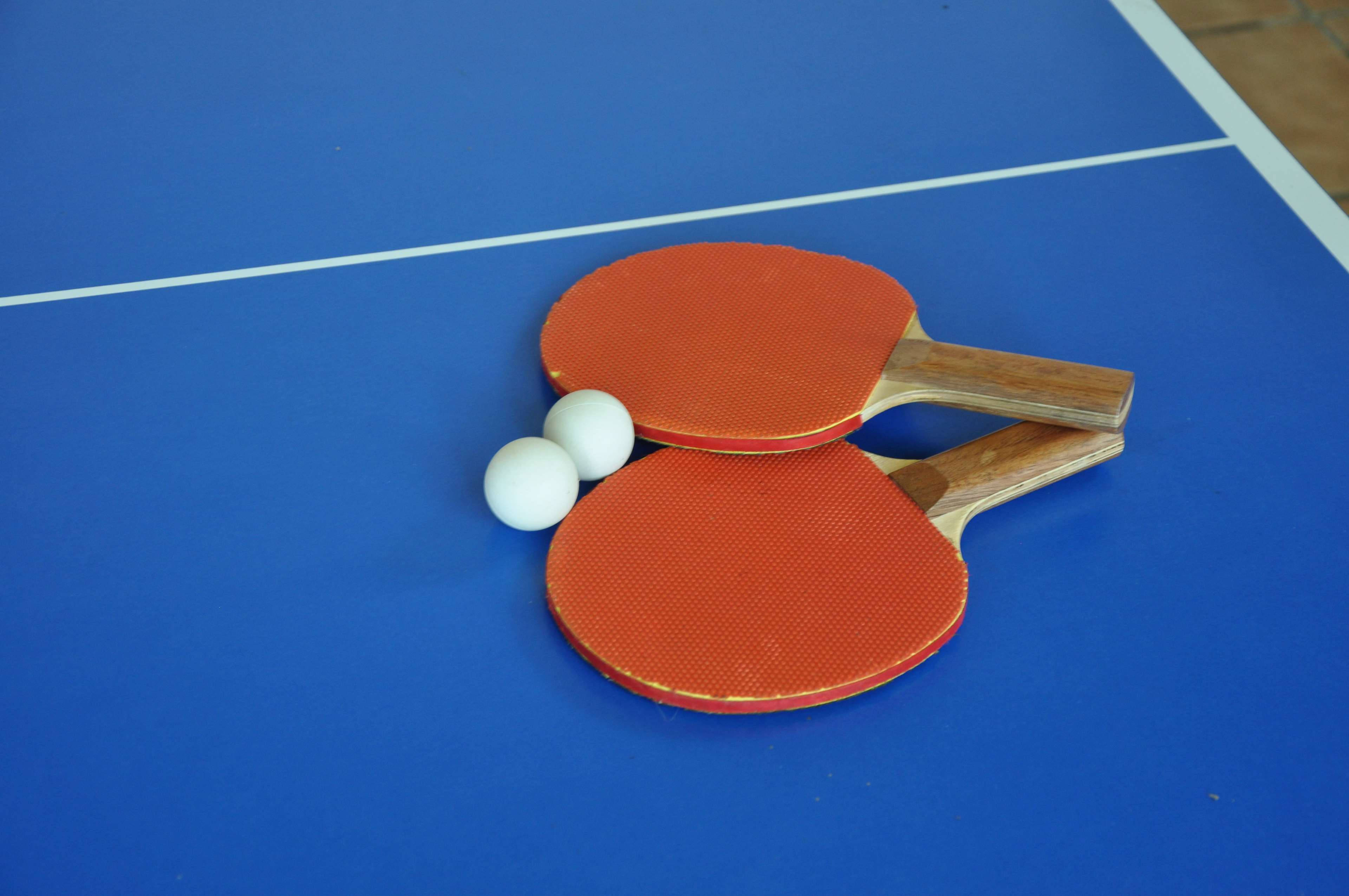 Table Tennis 桌布 壁紙 — 兩個紅色乒乓球拍和兩個白色球放在一張帶有白色線條的鮮藍色桌子上。
