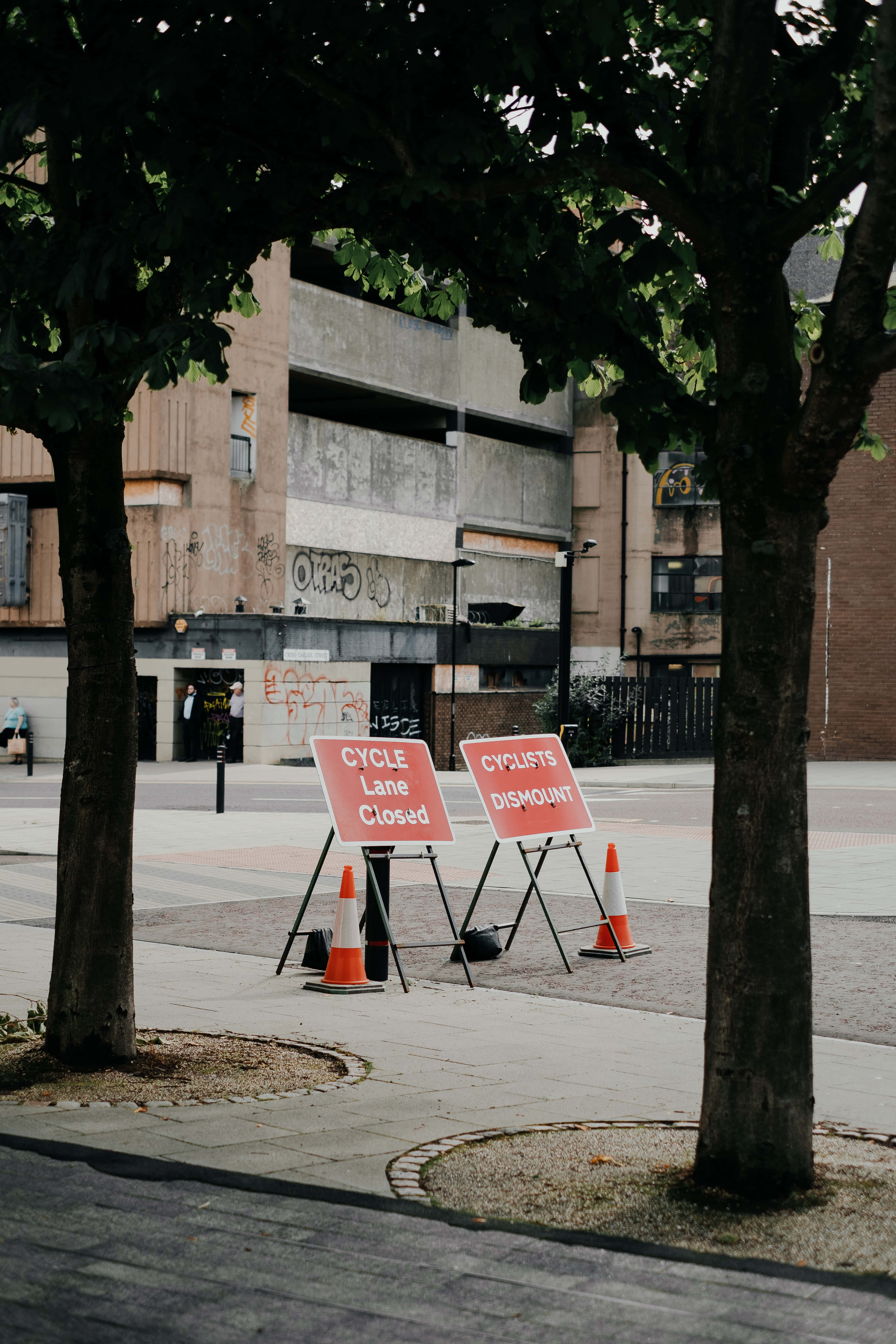 Signs 桌布 壁紙 — 兩個紅色標誌警告騎自行車者下車，因為自行車道在樹木茂盛和風化的城市建築附近關閉。