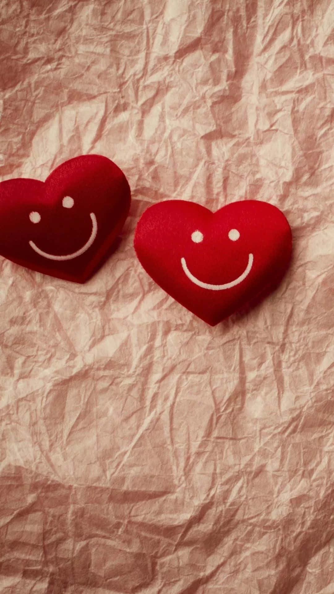 Cute Hearts 桌布 壁紙 — 兩個紅色氈製心形，帶有白色笑臉，放在皺巴巴的粉紅色紙上。