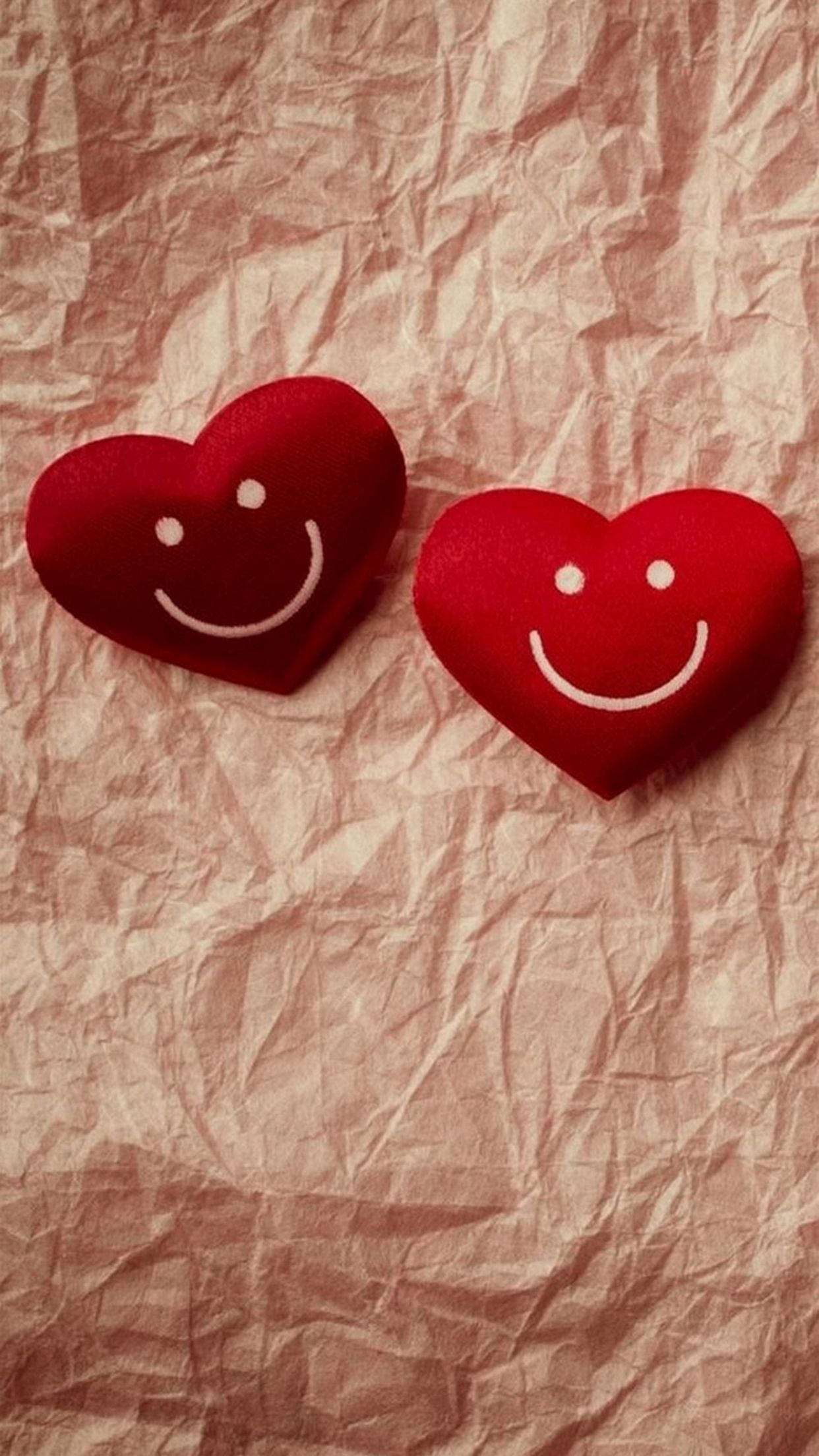 Love Phone 桌布 壁紙 — 兩個紅色氈製心形，帶有白色笑臉，放在皺巴巴的米色紙上。