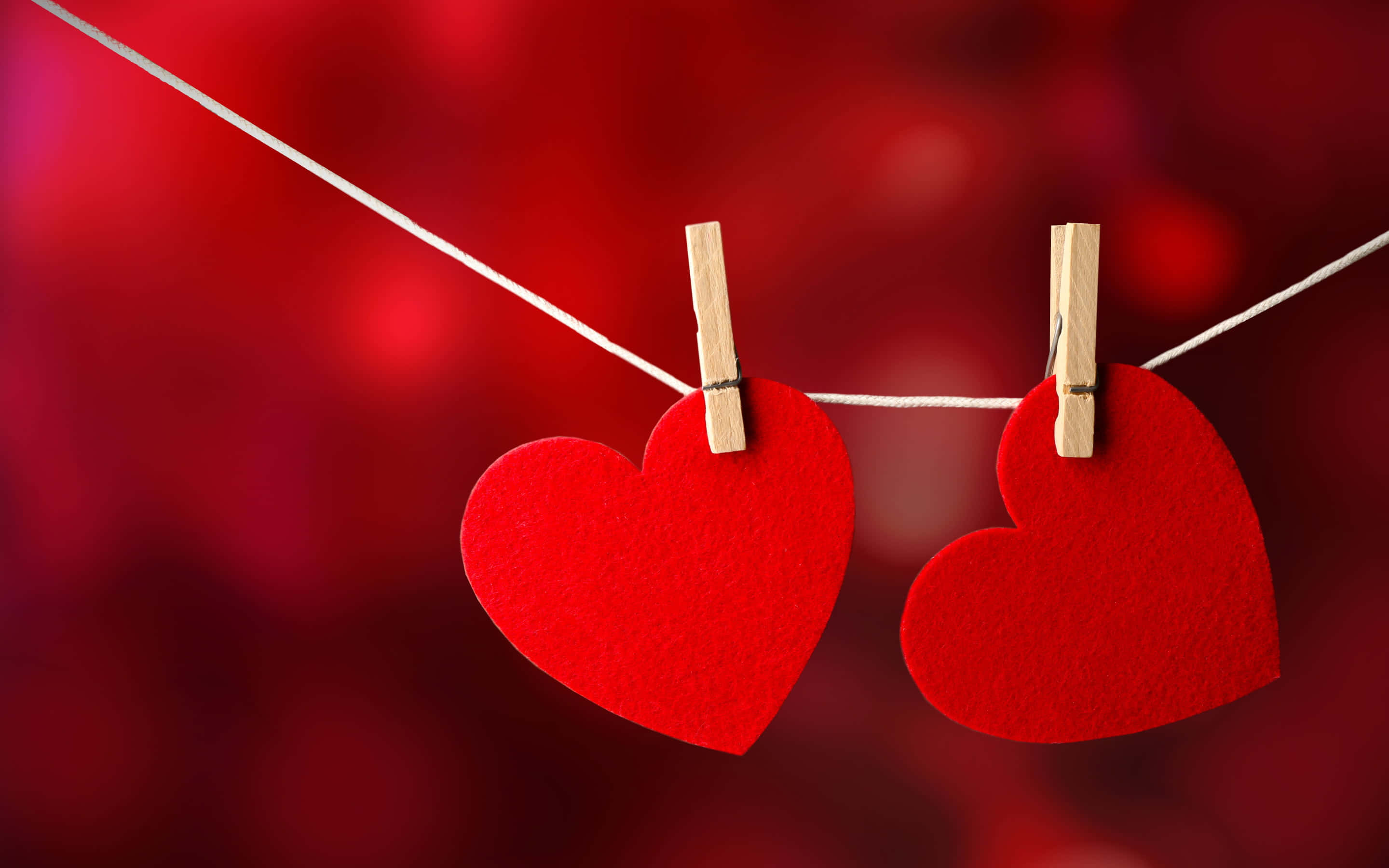 Aesthetic Heart 桌布 壁紙 — 兩個紅色氈製心形掛在一條白色繩子上，用木夾固定，背景是模糊的紅色。
