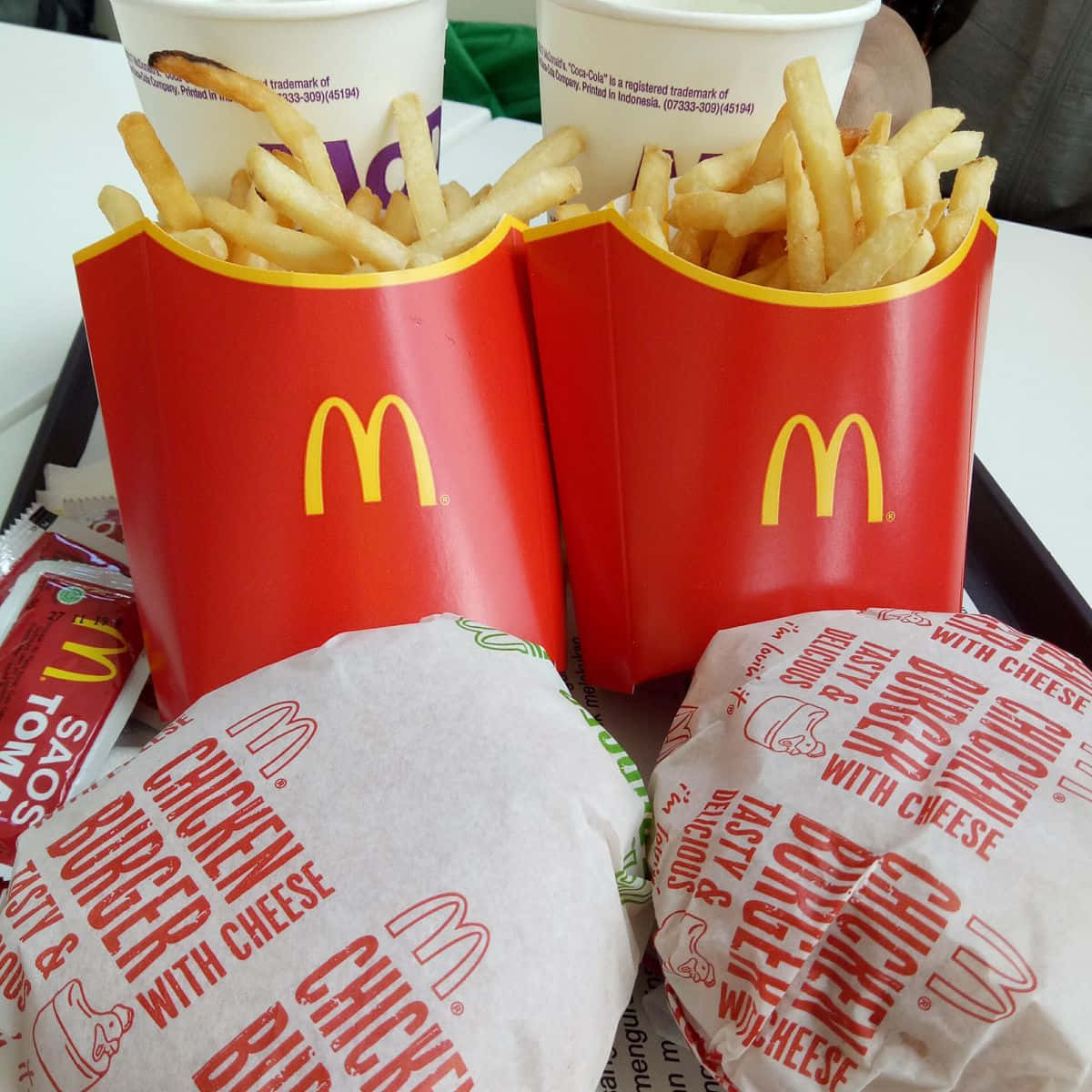 Mcdonalds Food 桌布 壁紙 — 兩個紅色麥當勞薯條盒和包裝雞肉漢堡放在托盤上，附有醬料包和飲料。