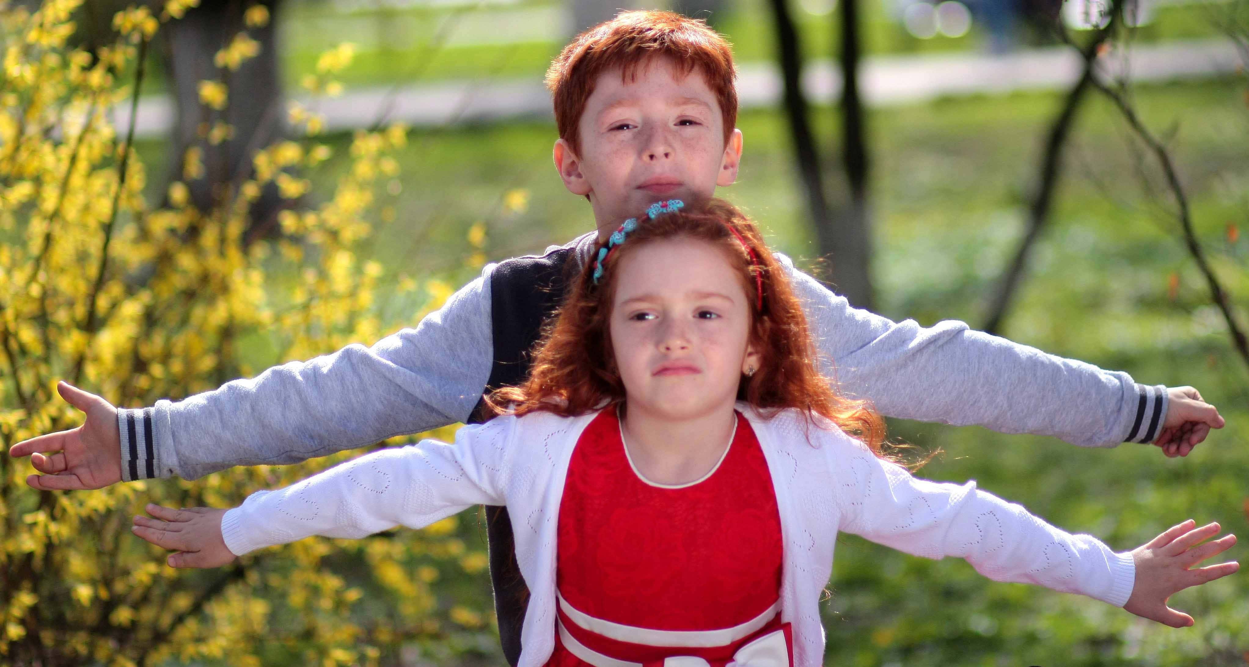 Brother And Sister 桌布 壁紙 — 兩個紅髮小孩在戶外張開雙臂，以盛開的黃色花朵和綠草為背景，頑皮地擺姿勢。