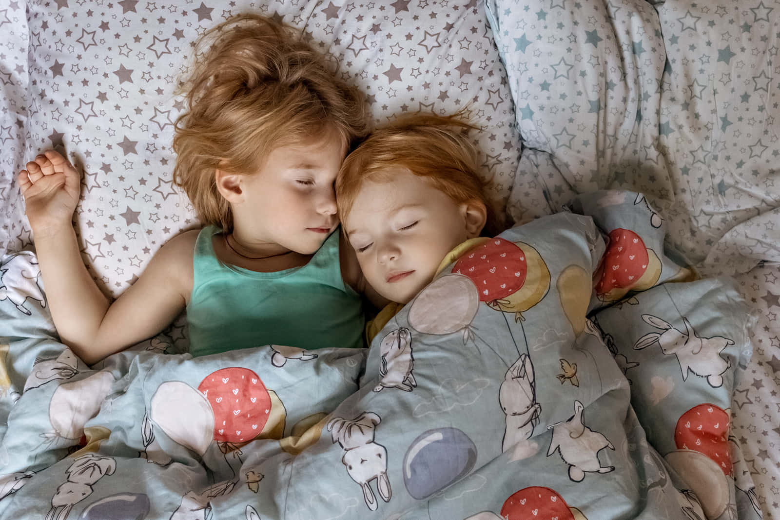 People Sleeping 桌布 壁紙 — 兩個紅髮的熟睡孩子，在星星圖案的床單上，蓋著印有兔子和氣球的毯子，安詳地休息。