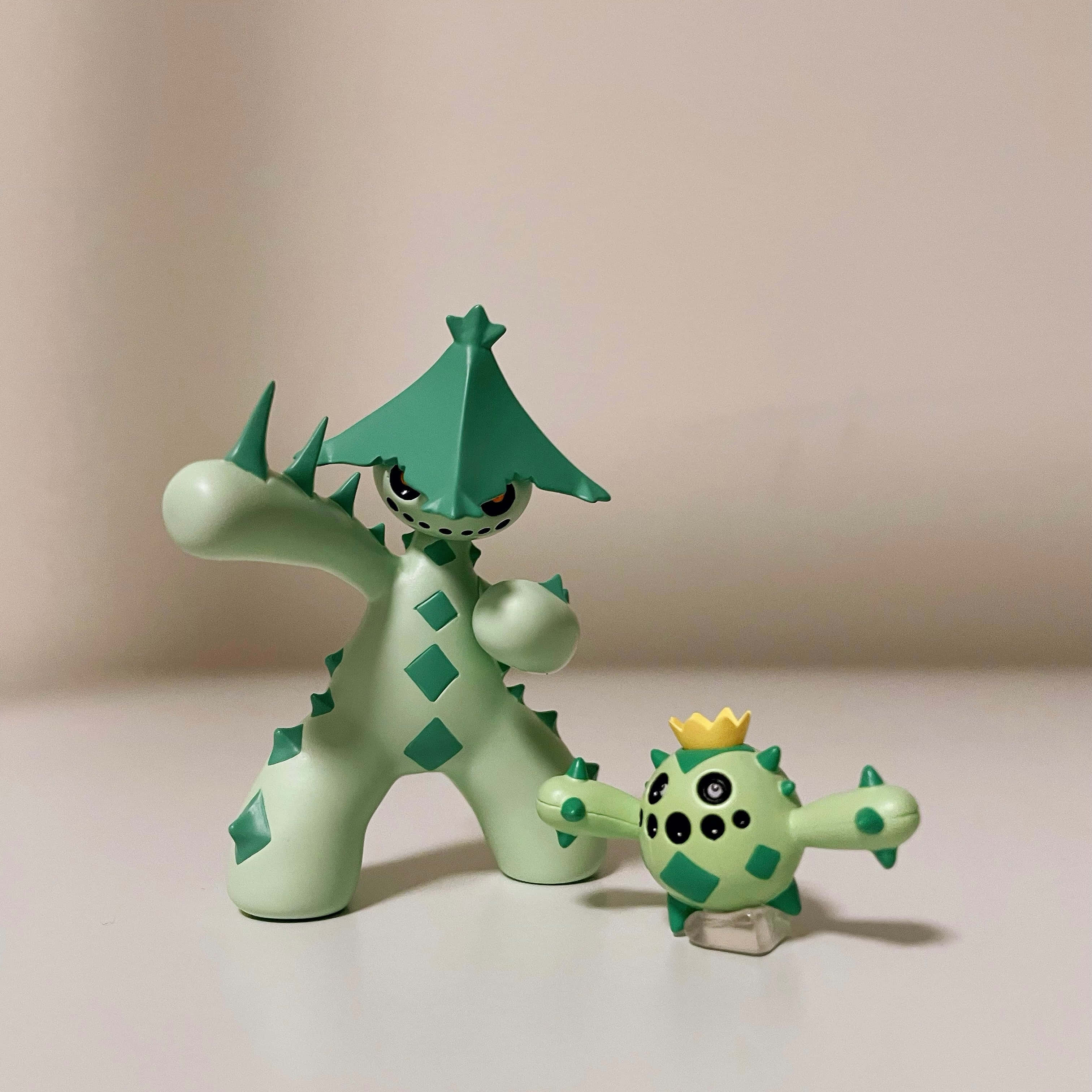 3D 桌布 壁紙 — 兩個綠色寶可夢公仔，一個高的戴帽子，一個小的戴皇冠，站在純白表面上。