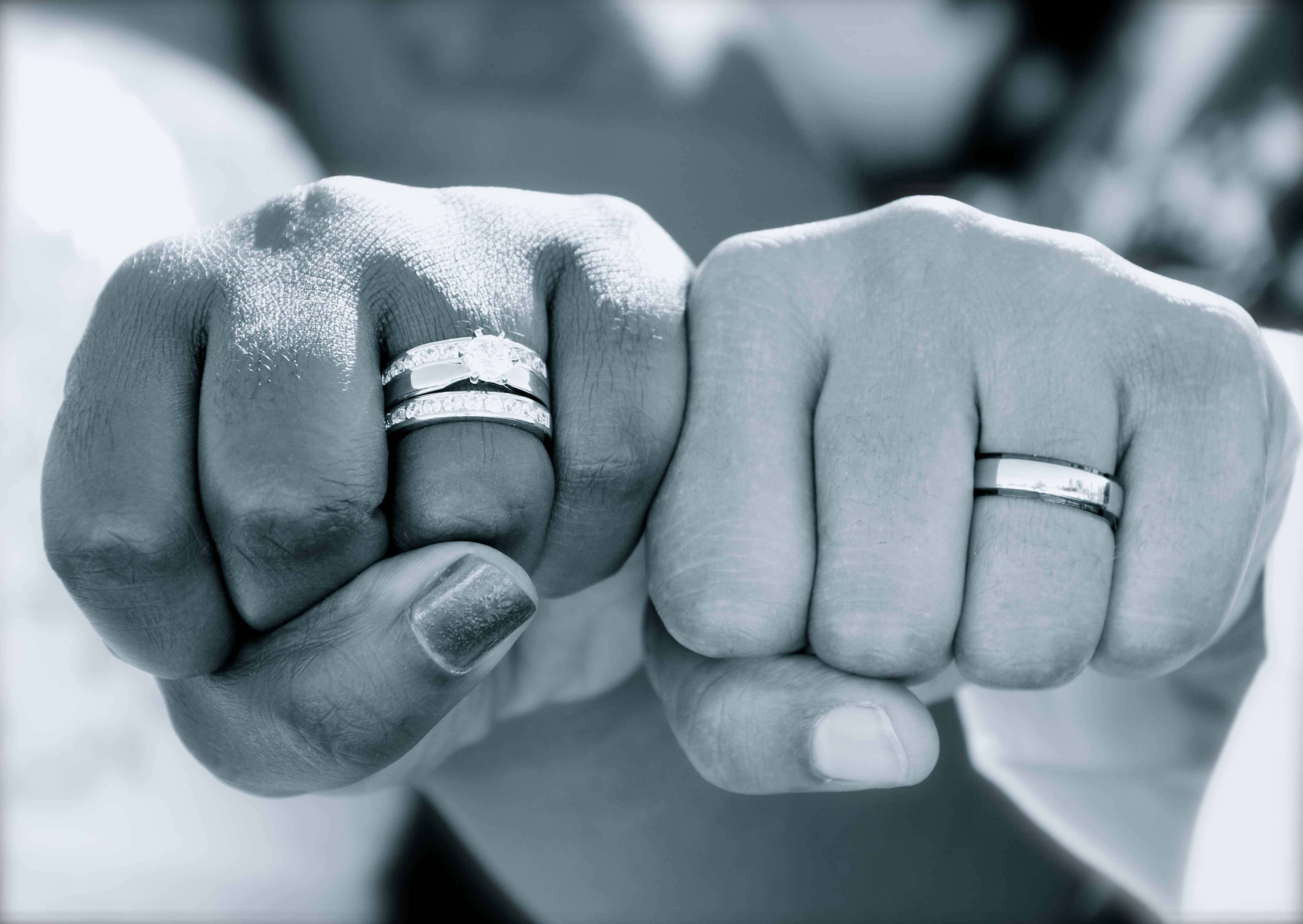 結婚戒指 桌布 壁紙 — 兩個緊握的拳頭，食指上戴著結婚戒指，在單色特寫中互相按壓。
