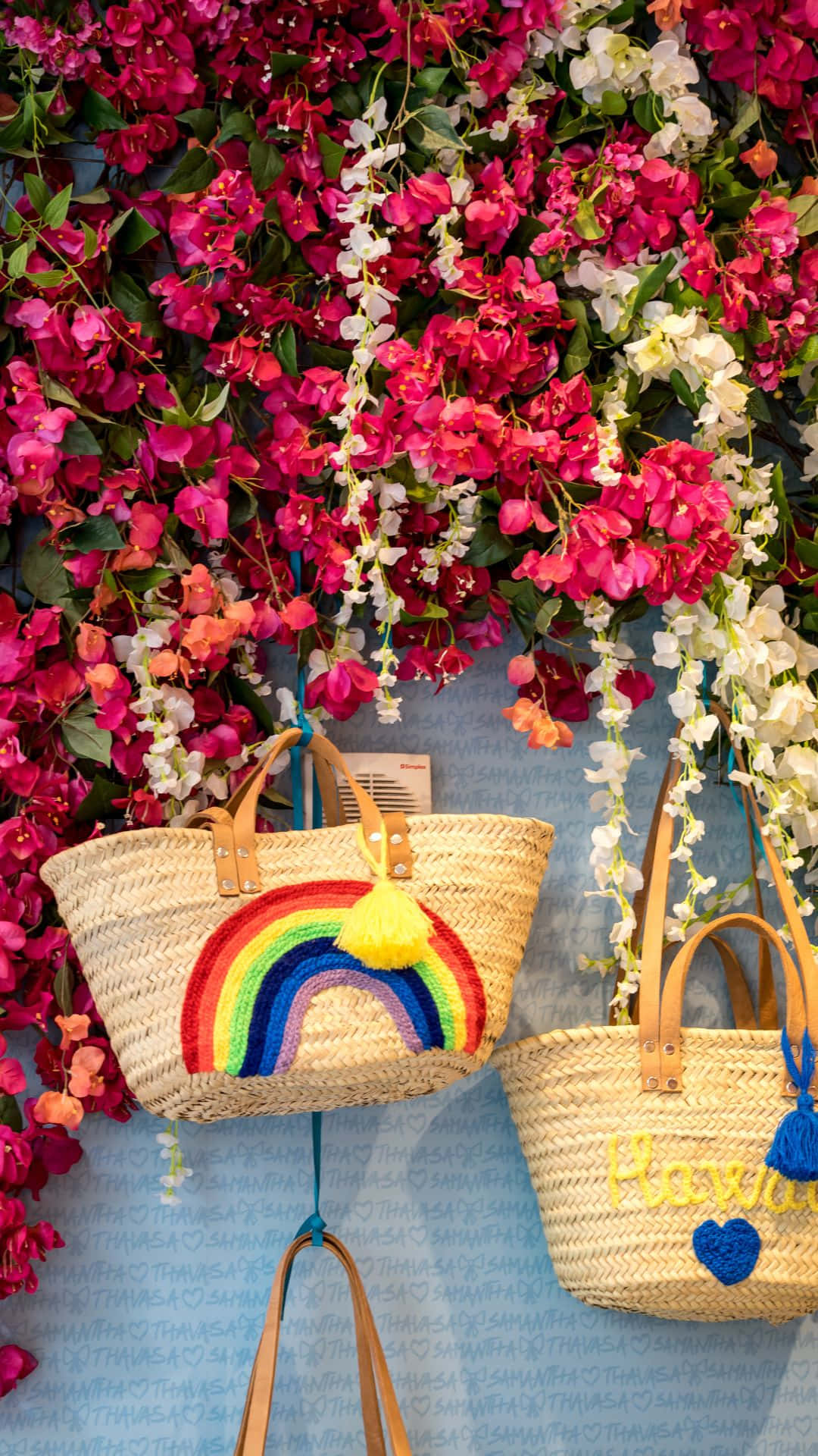 夏威夷 桌布 壁紙 — 兩個編織草袋，帶有彩虹和「夏威夷」刺繡，掛在充滿活力的粉紅色和白色九重葛花牆上。
