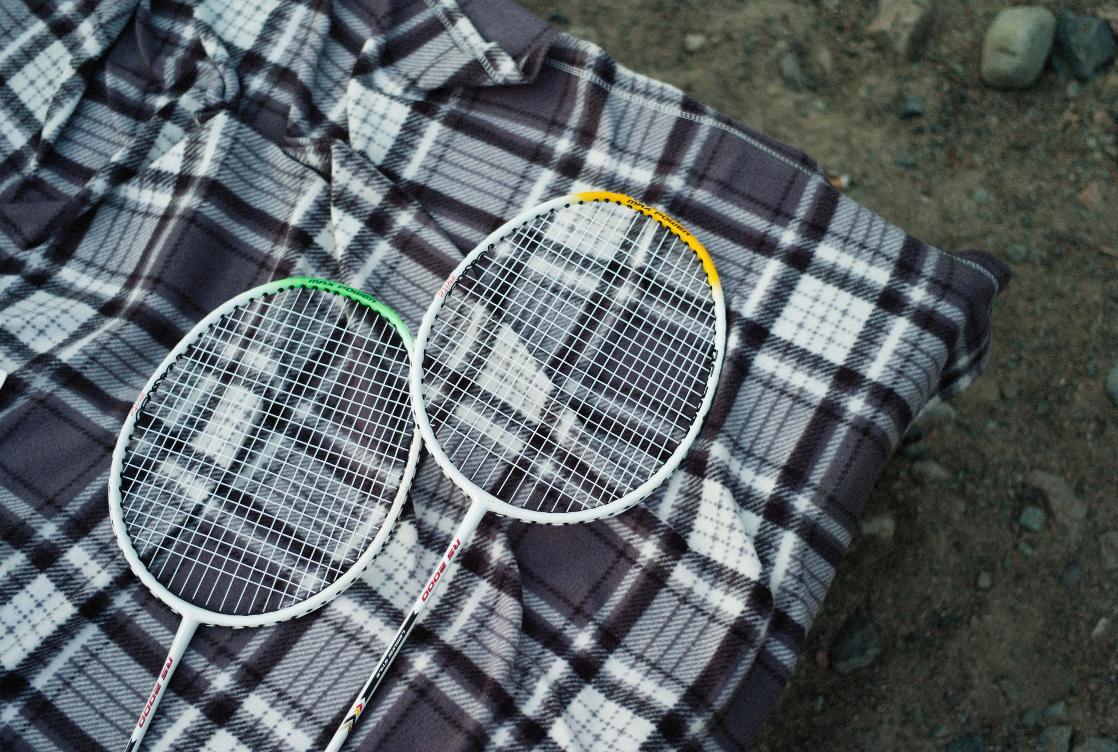 Badminton 桌布 壁紙 — 兩個羽毛球拍放在鋪在碎石地上的格子毯上。