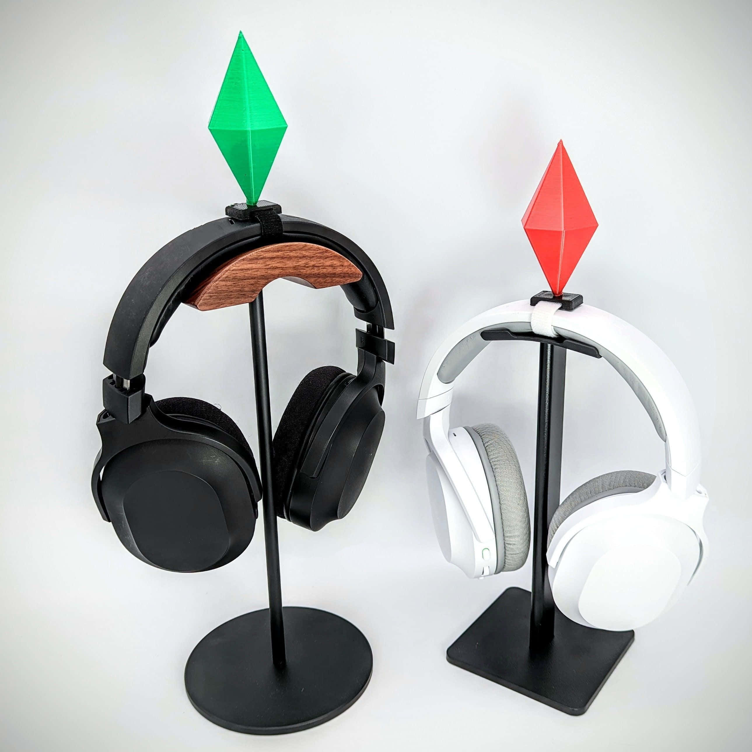 Gaming Accessories 桌布 壁紙 — 兩個耳機，一個黑色一個白色，展示在極簡風格的支架上，支架頂部有綠色和紅色的寶石形狀，背景為純白色。