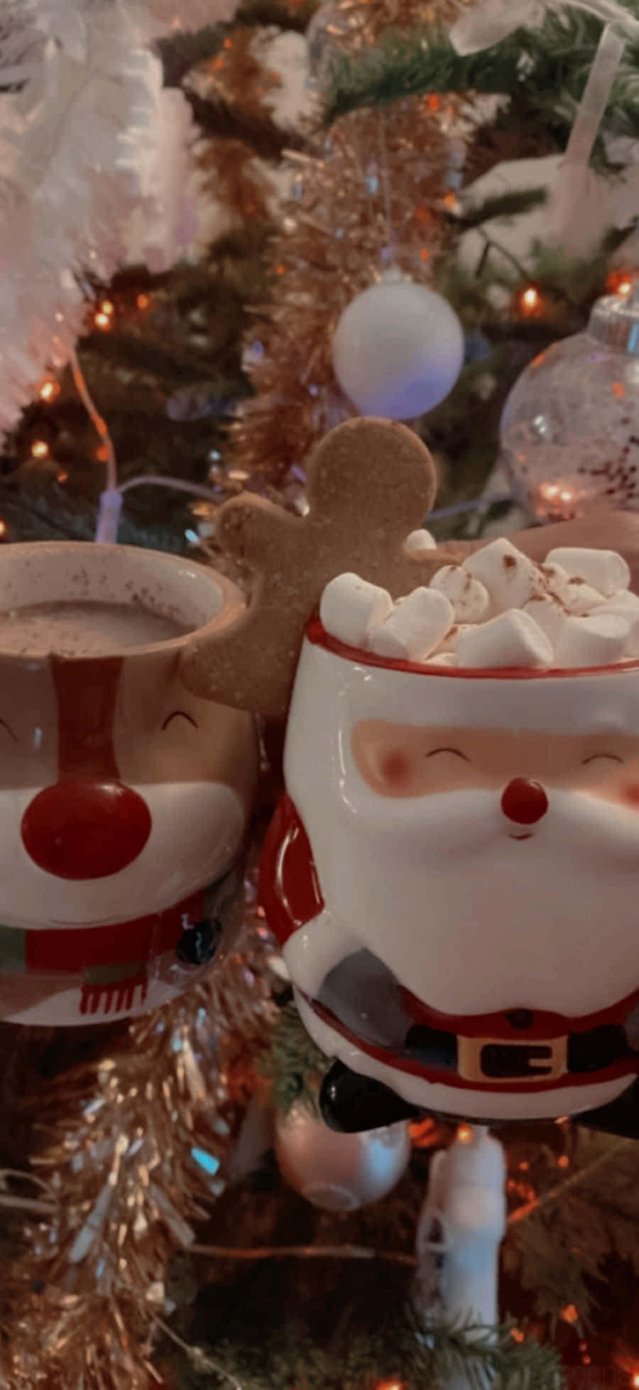 Tumblr Christmas 桌布 壁紙 — 兩個聖誕老人和馴鹿形狀的節日陶瓷杯，依偎在閃爍的聖誕樹裝飾和金屬絲之間。