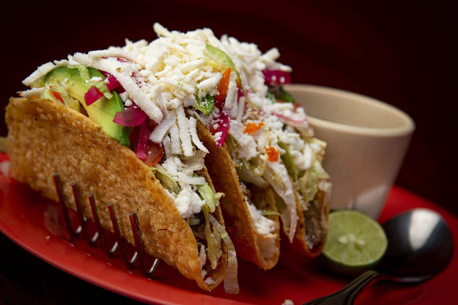 Mexican 桌布 壁紙 — 兩個脆皮墨西哥捲餅堆滿了切碎的起司、酪梨和醃洋蔥，放在紅色盤子上，旁邊有萊姆和湯匙。