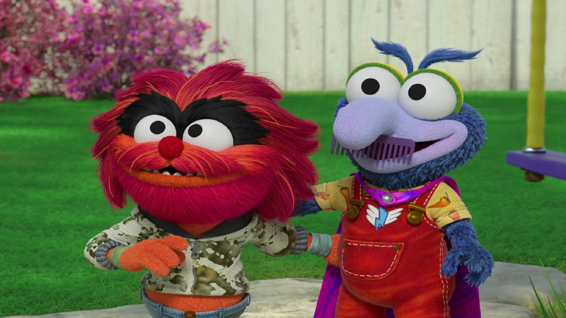 babies 桌布 壁紙 — 兩個色彩繽紛的Muppet角色站在陽光明媚的後院，身後有綠草和粉紅色的開花灌木。