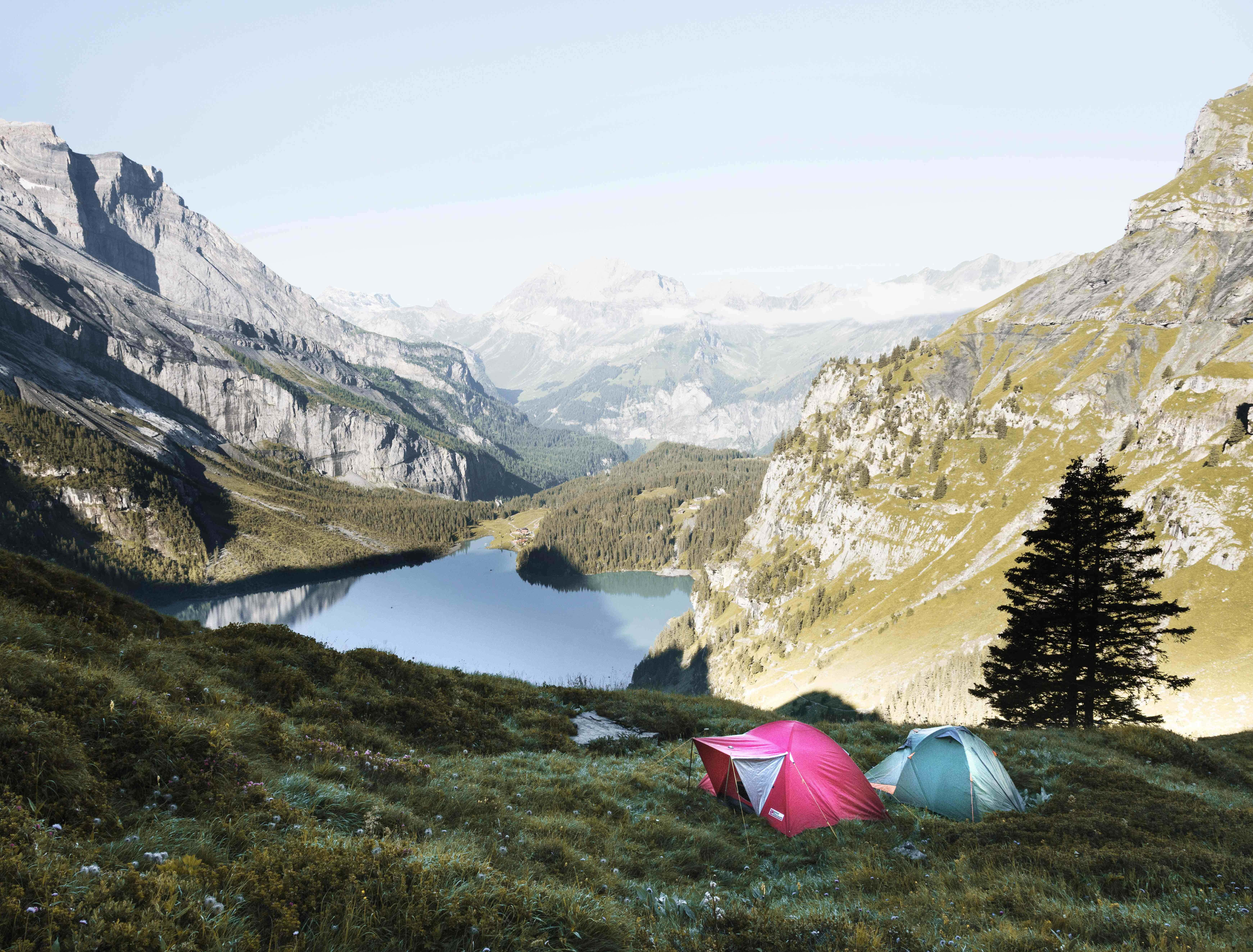 Camping 桌布 壁紙 — 兩個色彩繽紛的帳篷坐落在一個草坡上，俯瞰著一個寧靜的山間湖泊，遠處是崎嶇的山峰。