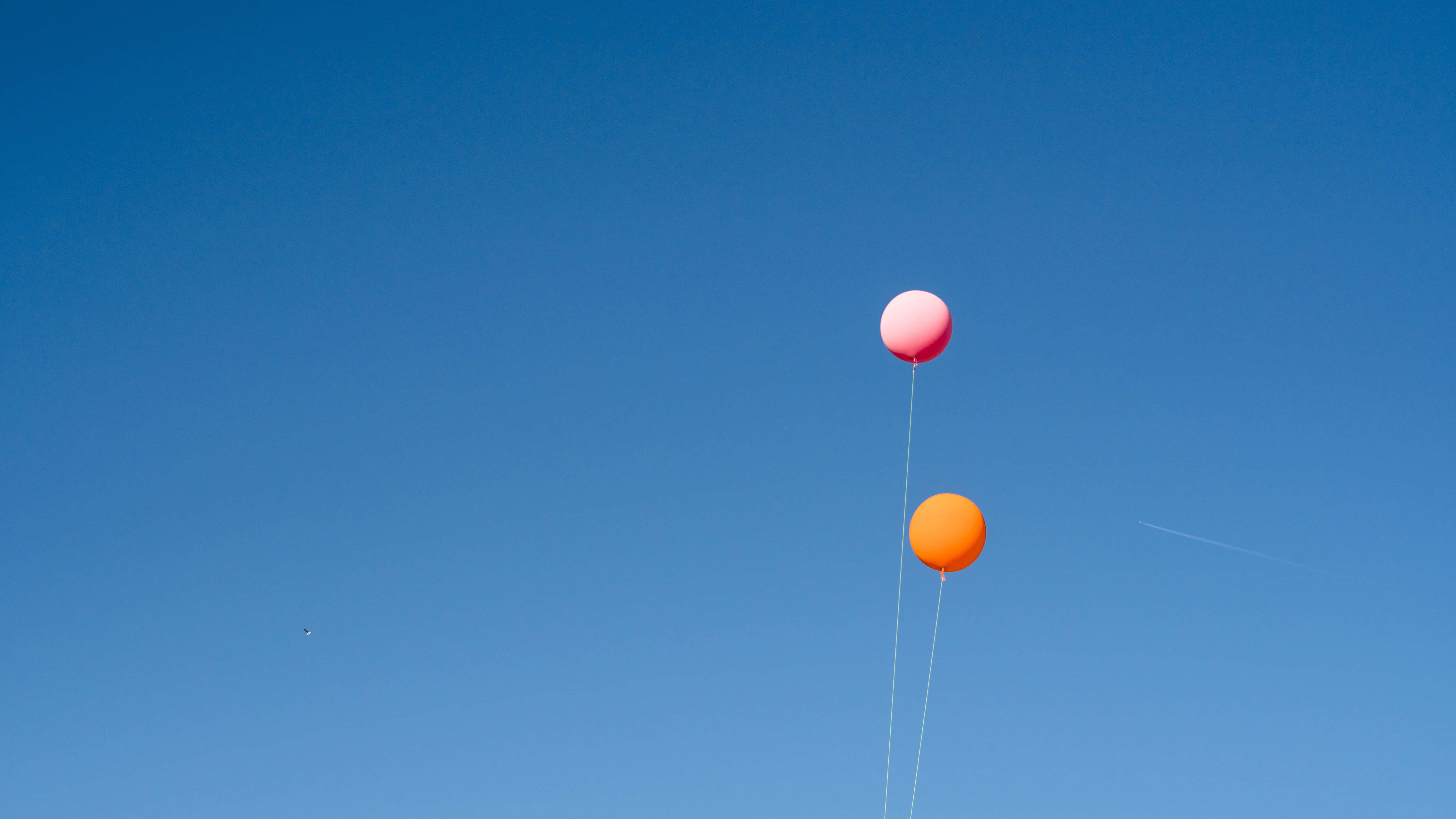 Balloons 桌布 壁紙 — 兩個色彩繽紛的氣球，粉紅色和橙色，在廣闊清澈的藍天中輕輕飄浮。