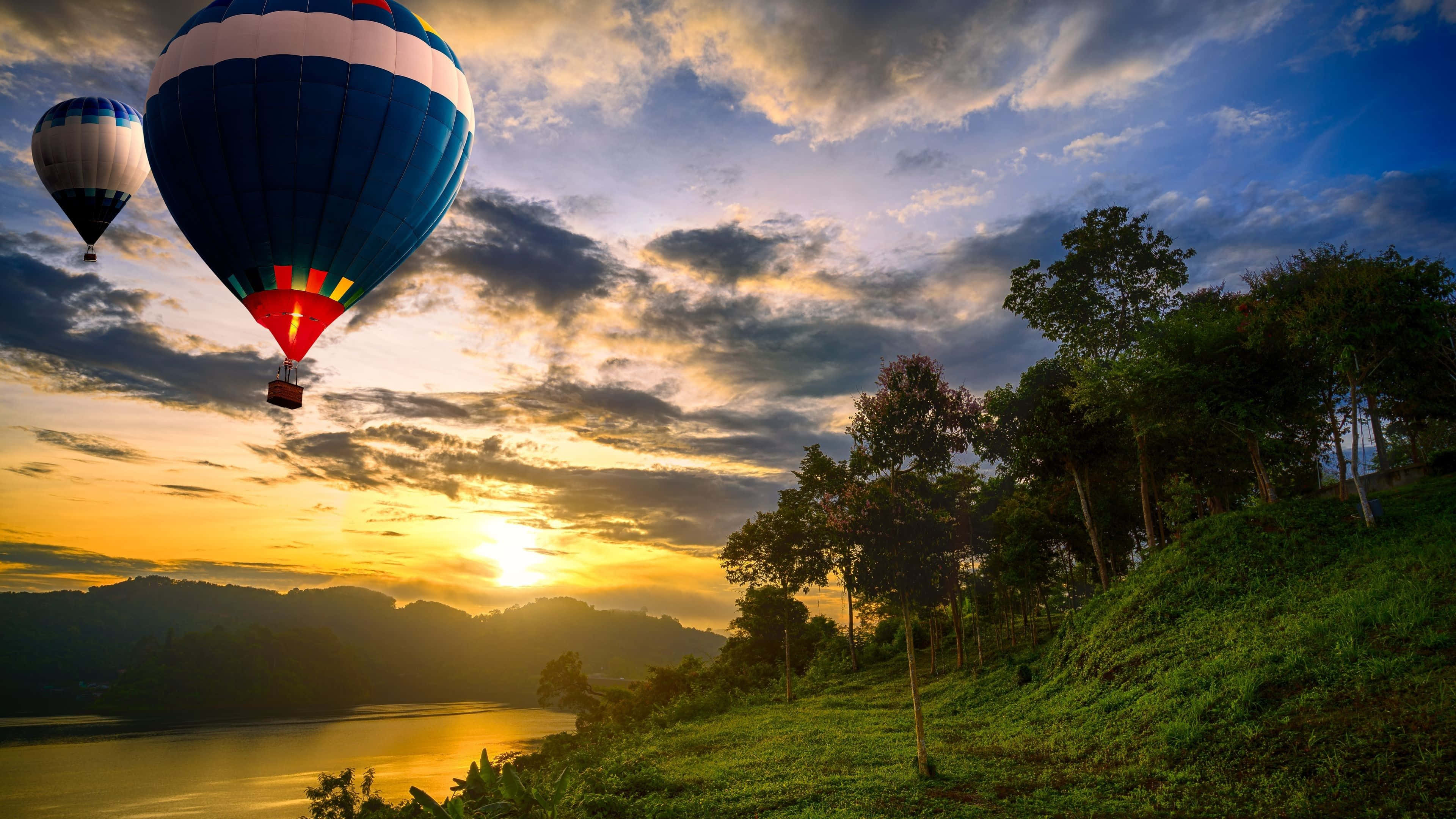 Hot Air Balloon 桌布 壁紙 — 兩個色彩繽紛的熱氣球在金色日落時分，飄過陽光普照的湖泊和樹木繁茂的山丘。