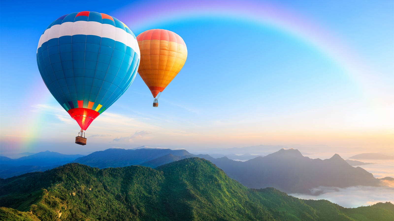 Hot Air Balloon 桌布 壁紙 — 兩個色彩繽紛的熱氣球在鬱鬱蔥蔥的綠色山脈上空翱翔，一道鮮豔的彩虹橫跨清澈的藍天。