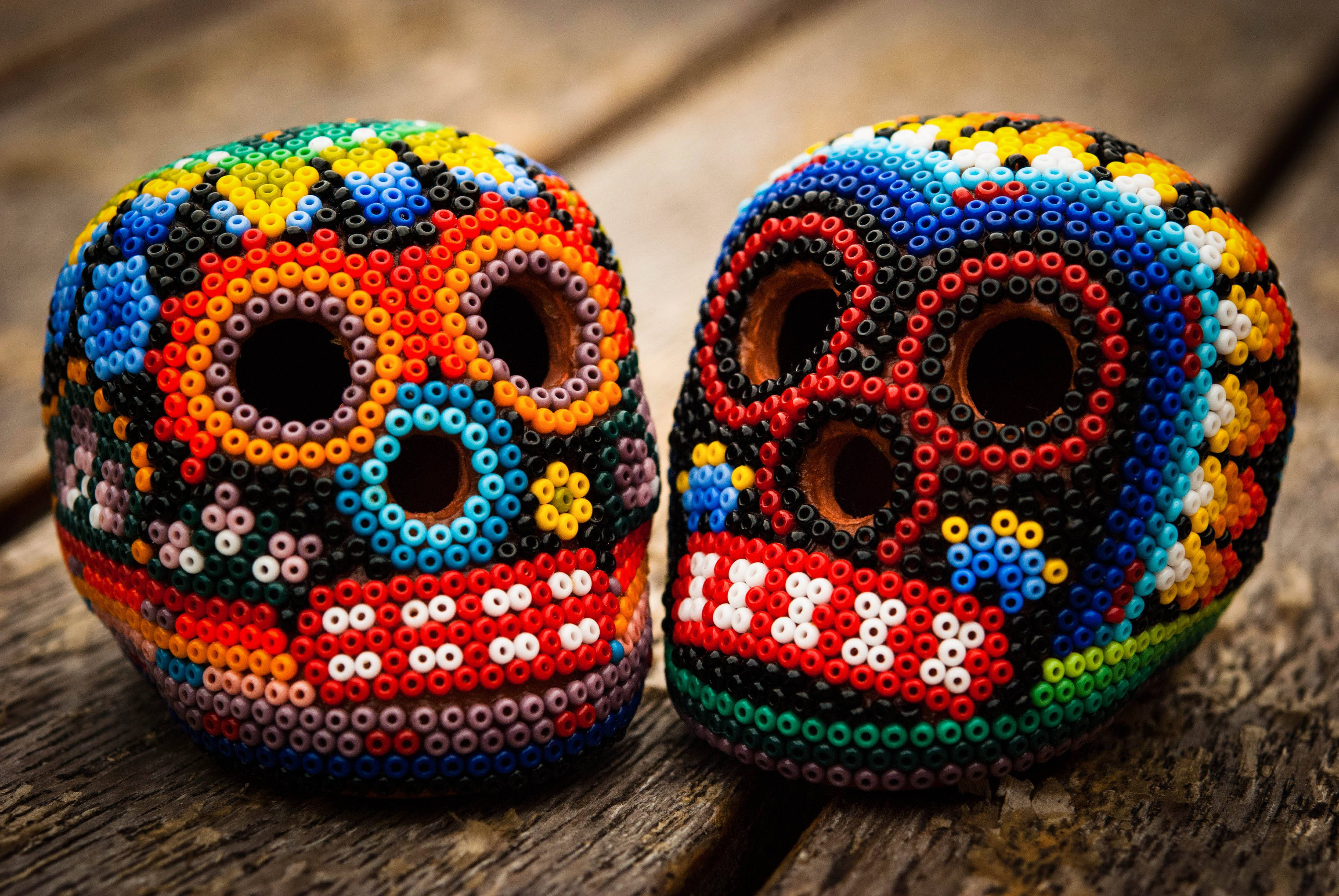 Chicano 桌布 壁紙 — 兩個色彩鮮豔的串珠糖骷髏頭放在風化木上，展現出複雜多彩的圖案和節日氣氛濃厚的墨西哥亡靈節藝術。