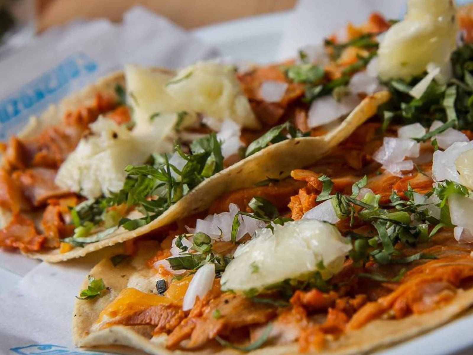 Mexican Food 桌布 壁紙 — 兩個色彩鮮豔的墨西哥烤豬肉塔可，上面放有鳳梨、香菜和洋蔥，放在鋪有紙的盤子上。