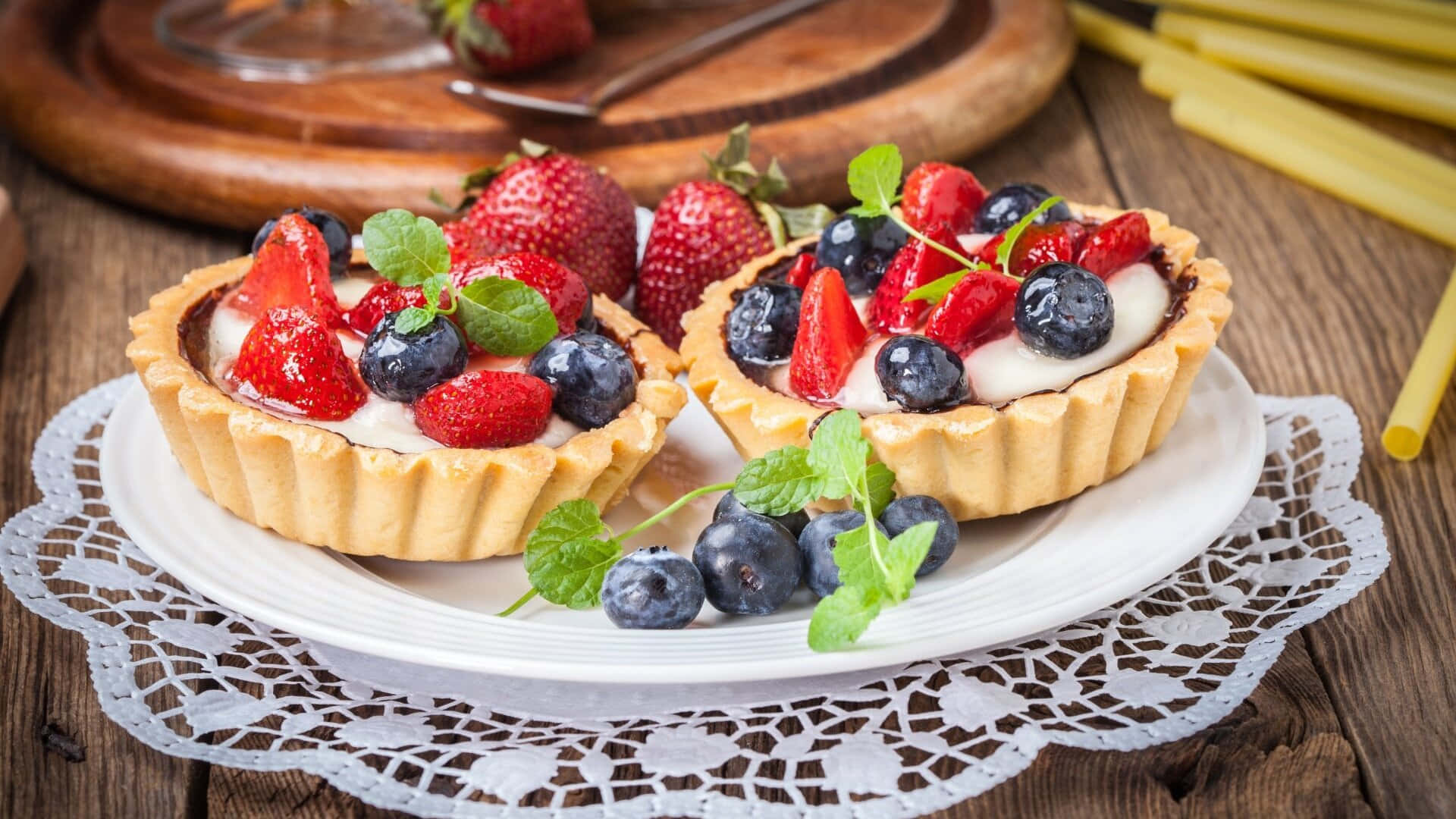 Desserts 桌布 壁紙 — 兩個莓果塔，上面鋪滿草莓、藍莓和薄荷，放在鄉村風格木桌上的蕾絲墊上。