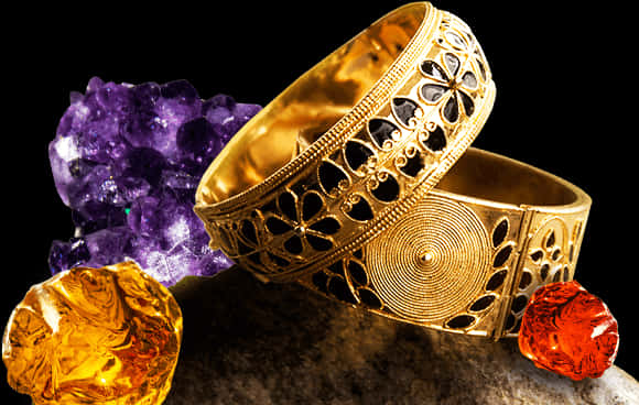 Gemstones 桌布 壁紙 — 兩個華麗的金手鐲帶有鏤空花紋，旁邊是充滿活力的紫水晶、黃水晶和紅玉髓寶石，放在深色紋理表面上。