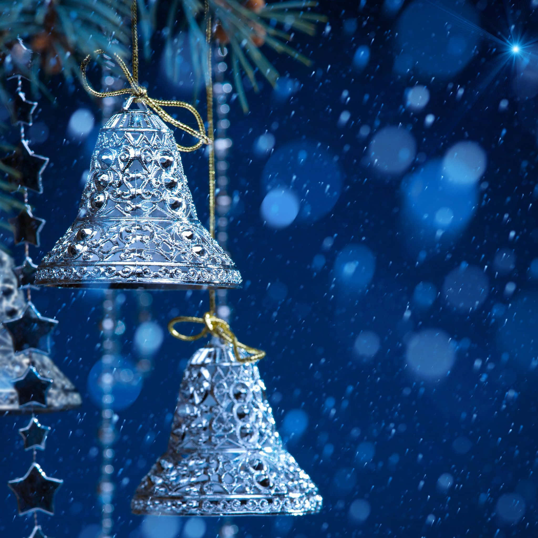 Christmas Ornament 桌布 壁紙 — 兩個華麗的銀色鈴鐺掛在松樹枝上，背景是雪白的藍色散景和星光。