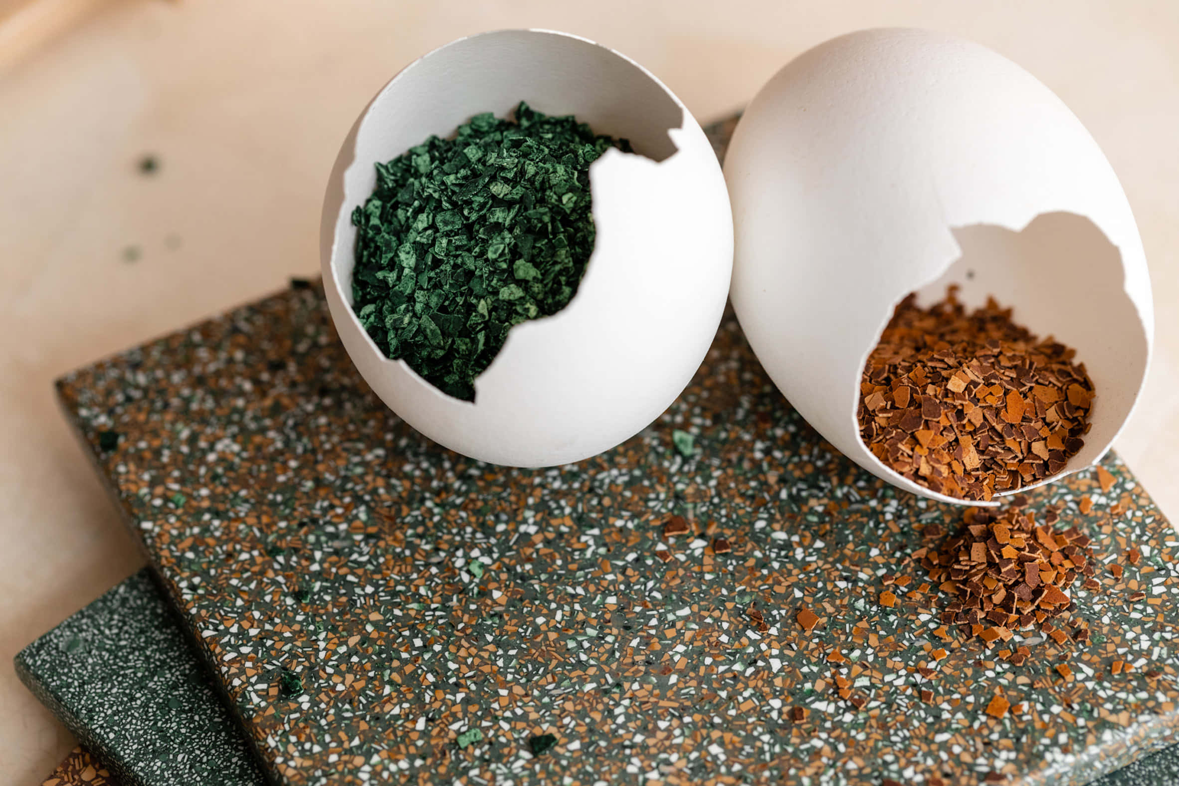 Eggshell 桌布 壁紙 — 兩個裂開的蛋殼在斑點水磨石表面上裝著充滿活力的綠色和棕色碎香草。