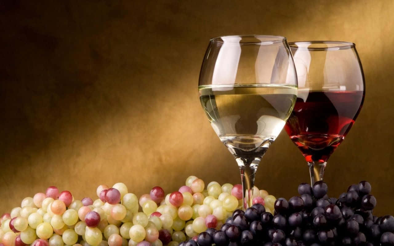 Grapes 桌布 壁紙 — 兩個裝滿白酒和紅酒的酒杯放在一堆綠色和紫色葡萄旁邊，背景是溫暖的金色。