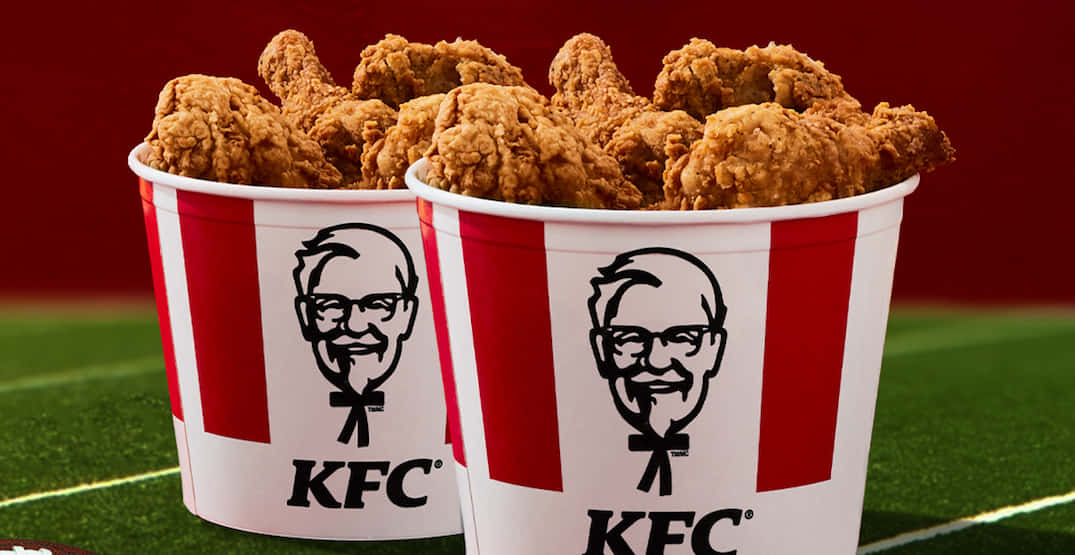 Kfc 桌布 壁紙 — 兩個裝滿金黃炸雞的KFC桶，溢出在綠色足球場上，背景為深紅色。