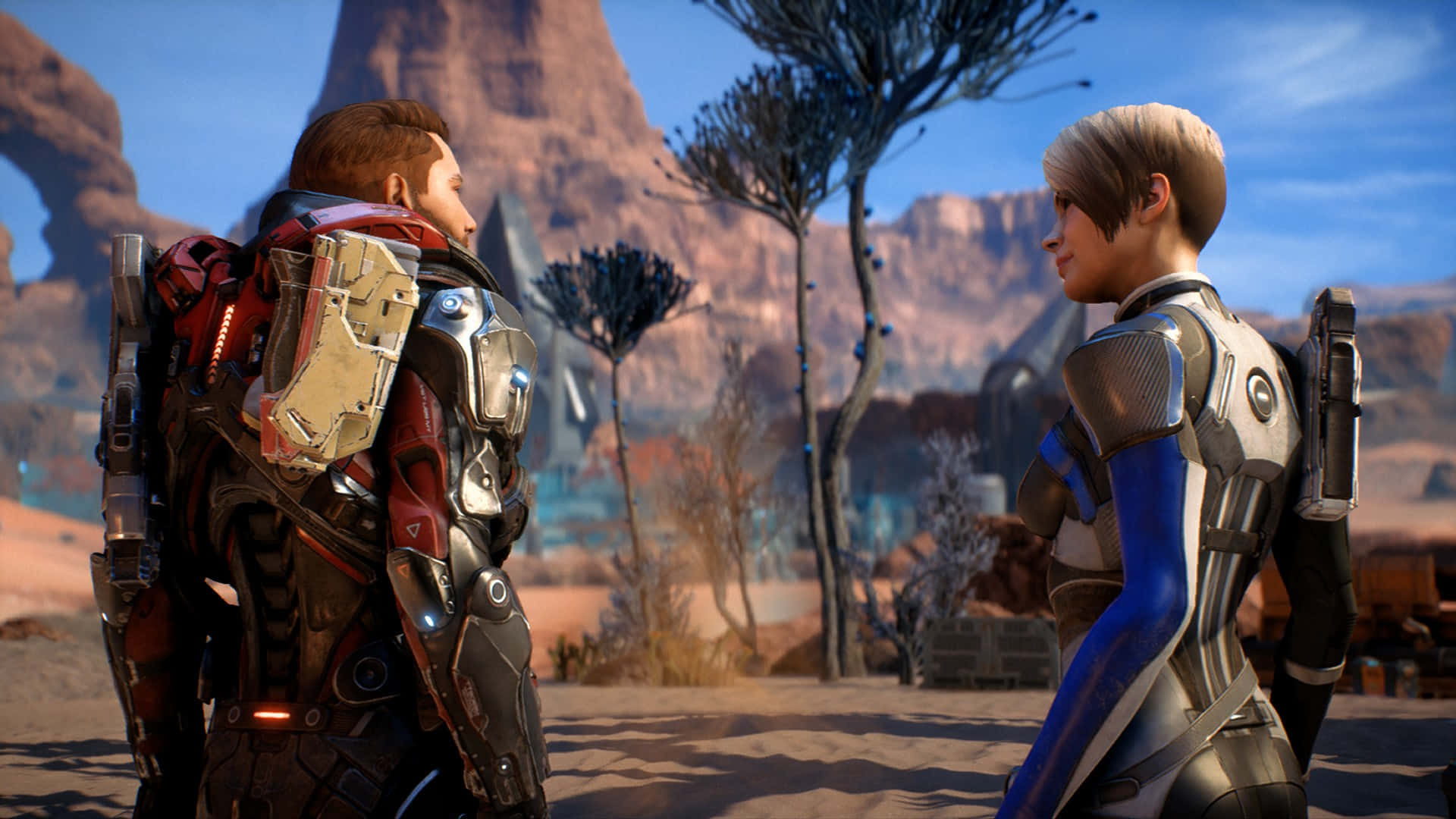 Mass Effect Andromeda 桌布 壁紙 — 兩個裝甲角色在陽光明媚的外星沙漠中面對面，周圍有岩石形成和稀疏的藍葉樹木。
