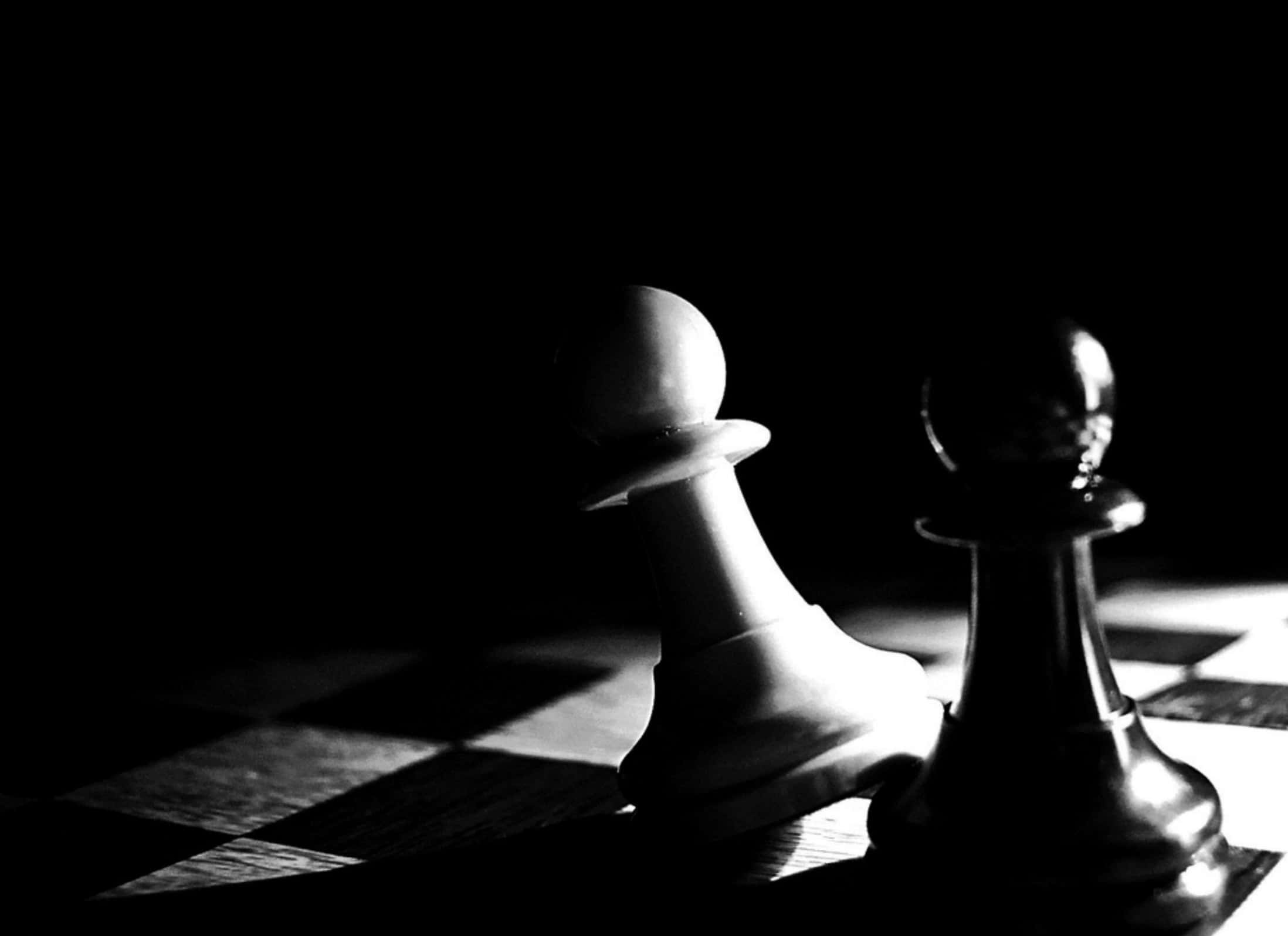 Cool Black And White 桌布 壁紙 — 兩個西洋棋兵卒在黑色虛空背景下，於棋盤上形成強烈對比，並處於戲劇性的聚光燈下。