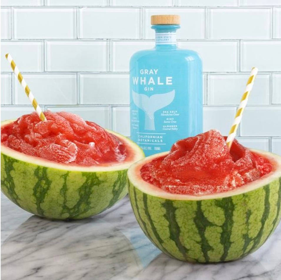alcohol 桌布 壁紙 — 兩個西瓜半邊裝滿紅色冰凍琴酒沙冰，放在大理石檯面上，旁邊有一支藍色琴酒瓶。