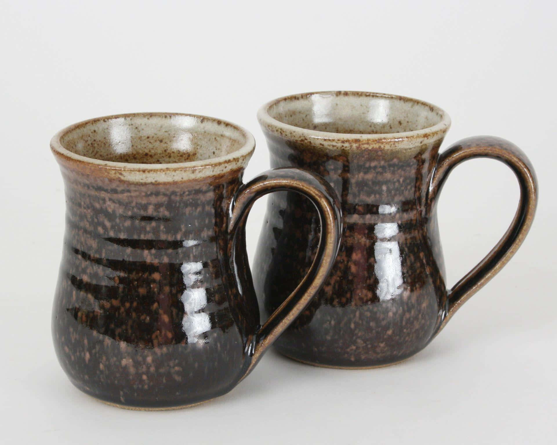 Ceramics 桌布 壁紙 — 兩個質樸的陶瓷杯，帶有斑駁的棕色釉料和彎曲的手柄，並排放在純白色背景上。