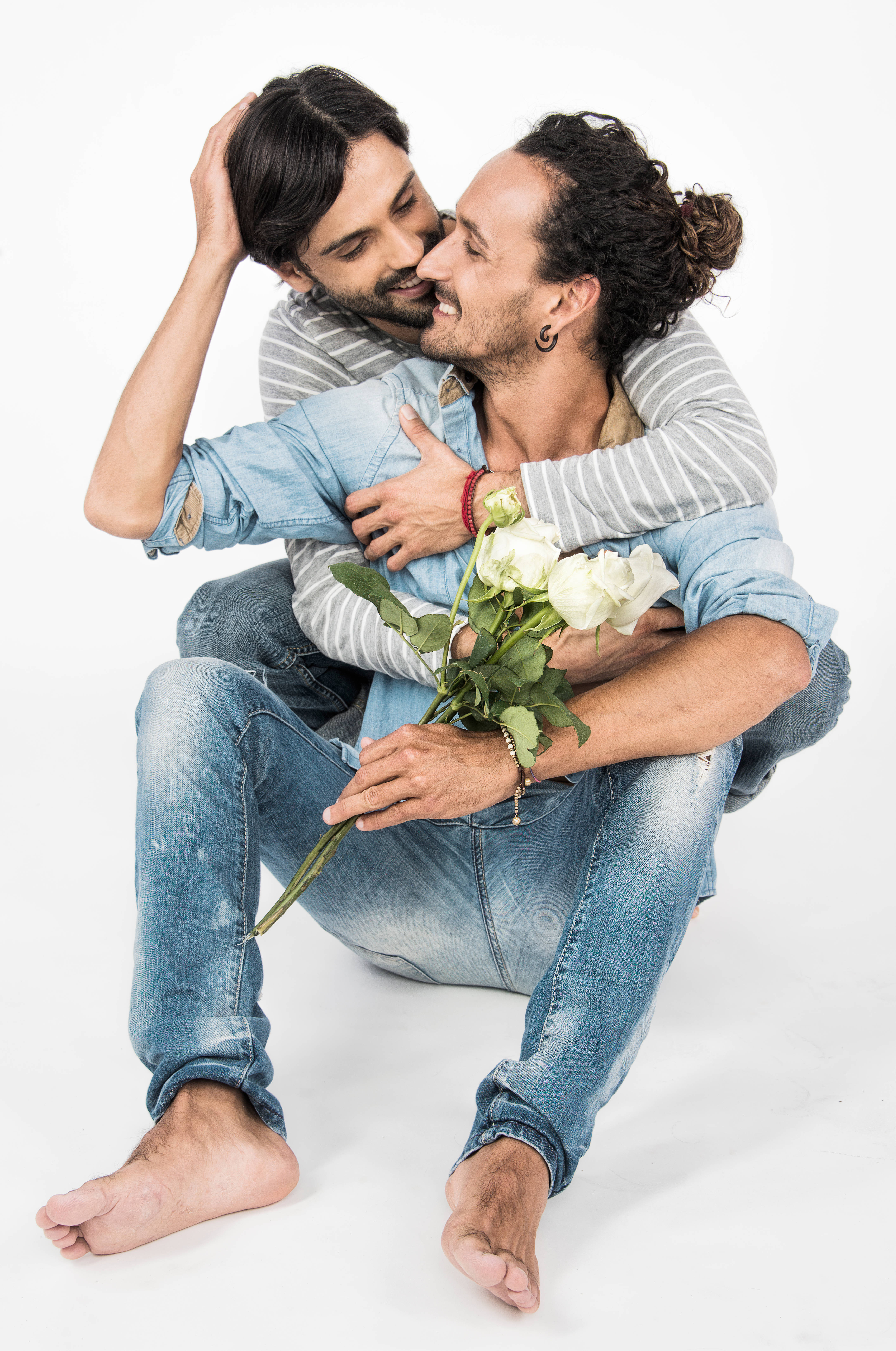 gay kiss 桌布 壁紙 — 兩個赤腳穿牛仔褲的男人在純白背景前親密擁抱，其中一人手持白玫瑰。