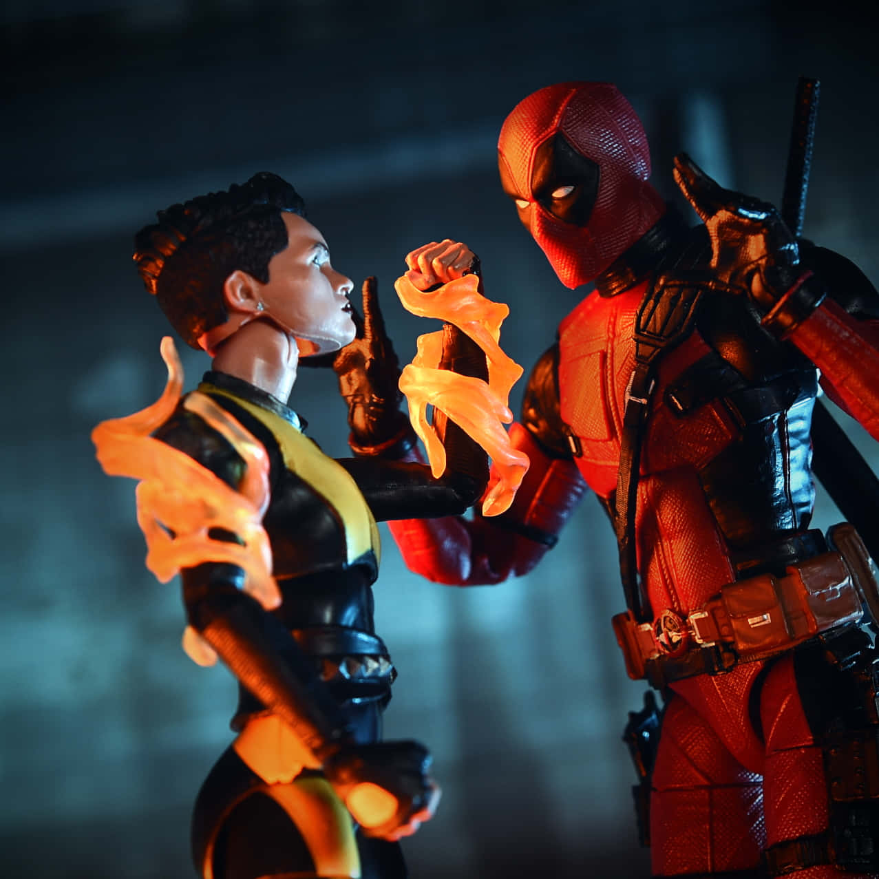Deadpool And Negasonic Teenage Warhead 桌布 壁紙 — 兩個超級英雄動作人偶，死侍和一個揮舞火焰的角色，在戲劇性的特寫中對峙，散發著熾熱的橙色能量。