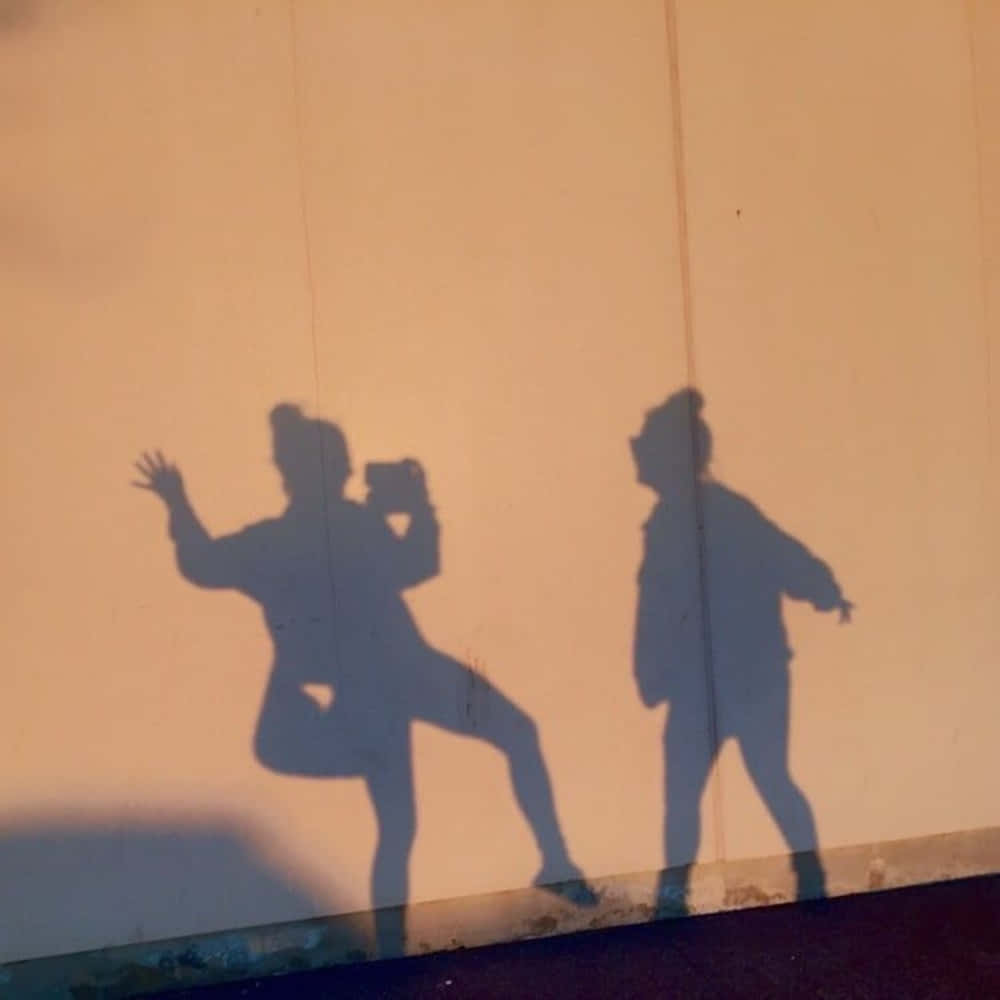 Best Friend Aesthetic 桌布 壁紙 — 兩個跳舞人物的動態剪影在黃金時段投射出長長的影子在暖色調的牆上。