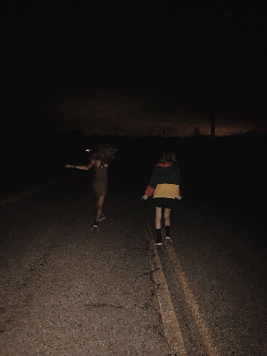 Grunge Emo Aesthetic 桌布 壁紙 — 兩個身影在夜晚沿著黑暗的鄉村道路走遠，地平線上有微弱的橙色光芒。