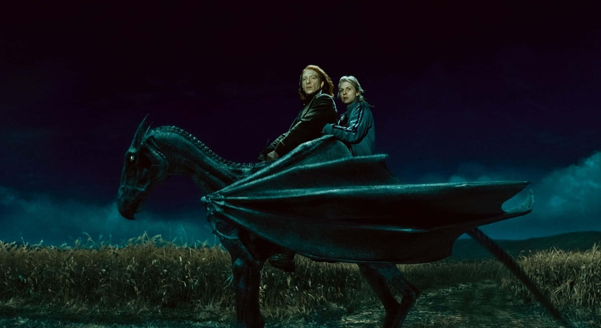 Thestral 桌布 壁紙 — 兩個身影騎著一條暗黑巨龍，在深藍色天空下，穿越暴風雨之夜，飛越一片高草田野。