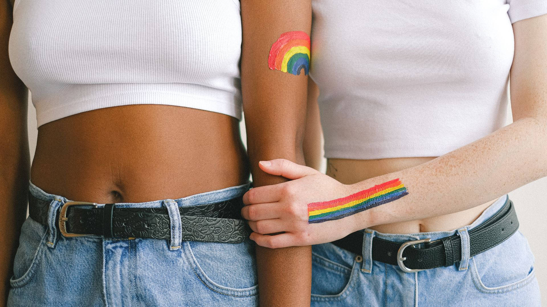 Subtle Lgbt 桌布 壁紙 — 兩個身穿白色短上衣和牛仔褲的人，手臂上裝飾著象徵LGBTQ+驕傲的彩虹臨時紋身。