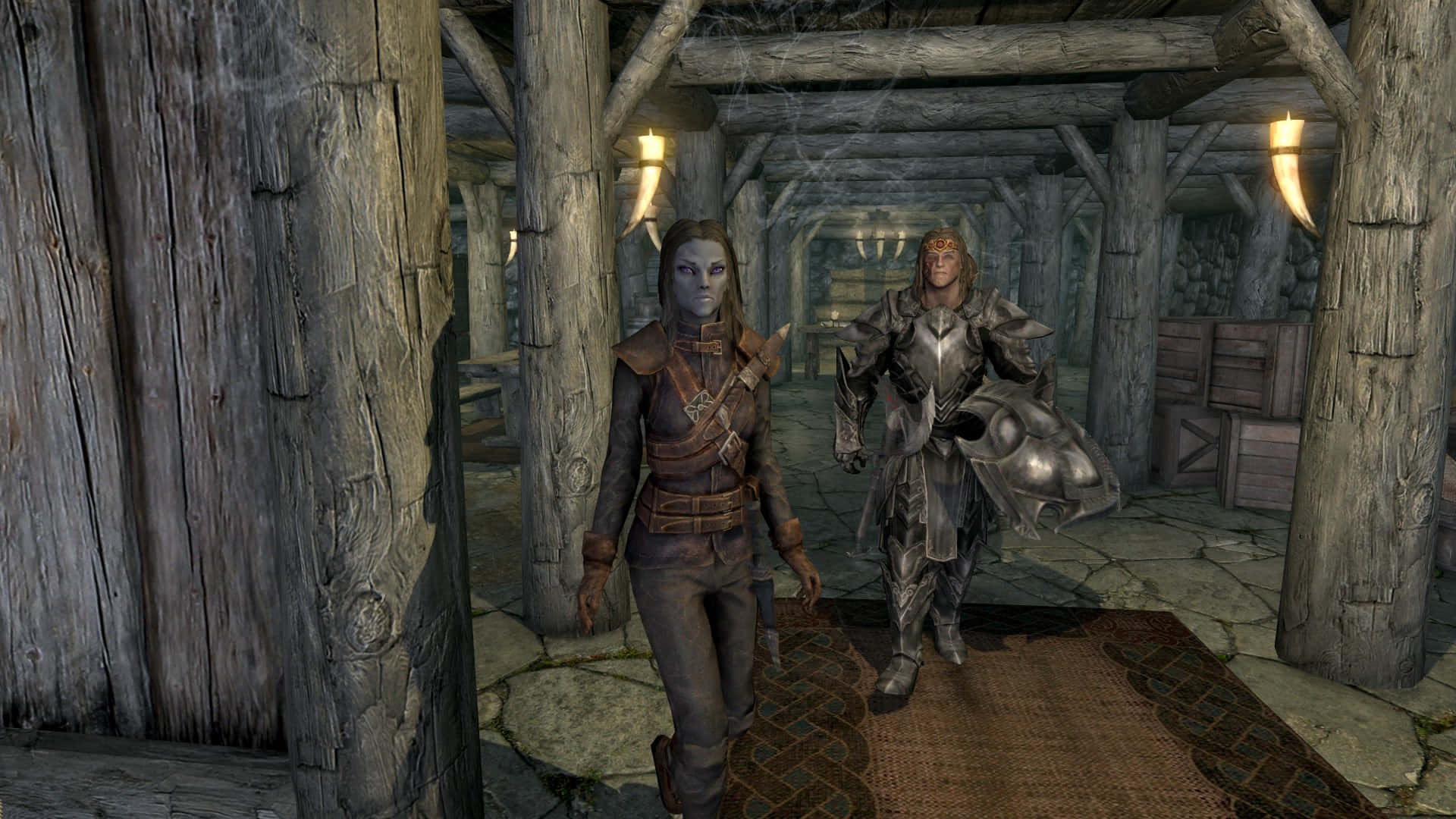 Skyrim Karliah 桌布 壁紙 — 兩個身穿盔甲的奇幻角色穿過一個由掛著火炬照亮的質樸木製大廳。