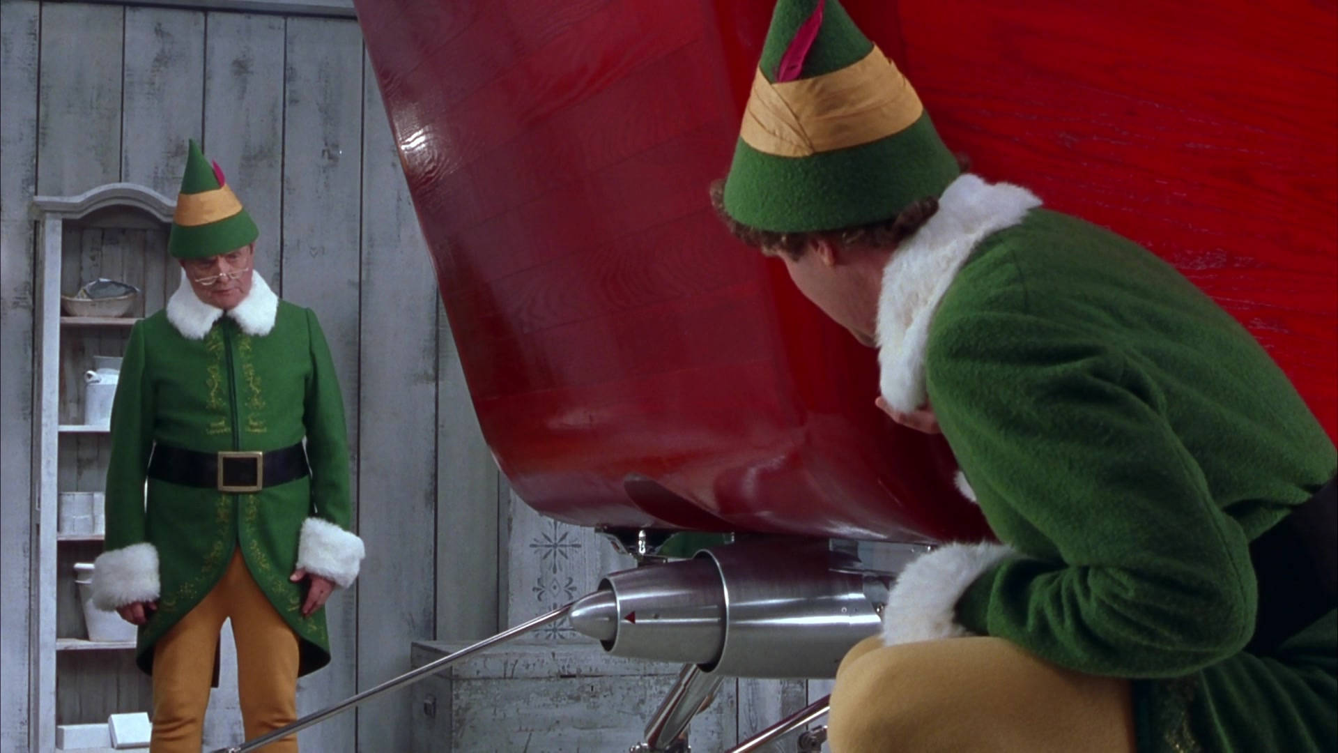 Elf Movie 桌布 壁紙 — 兩個身穿綠色服裝的精靈在質樸的木工作坊裡修理紅色雪橇。
