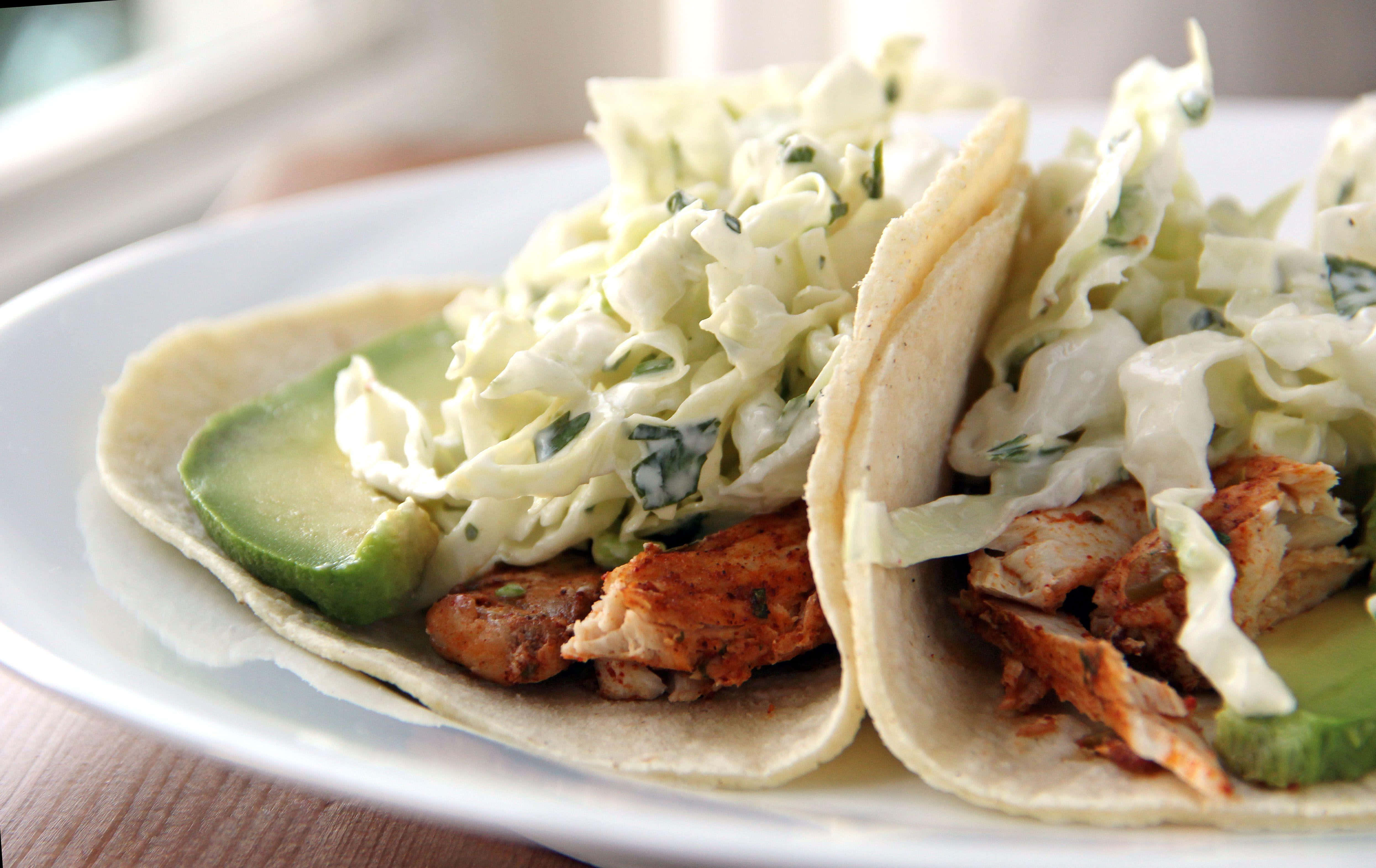 Taco 桌布 壁紙 — 兩個軟玉米餅，內餡有雞絲、酪梨和高麗菜沙拉，放在白色盤子上，背景是木桌。