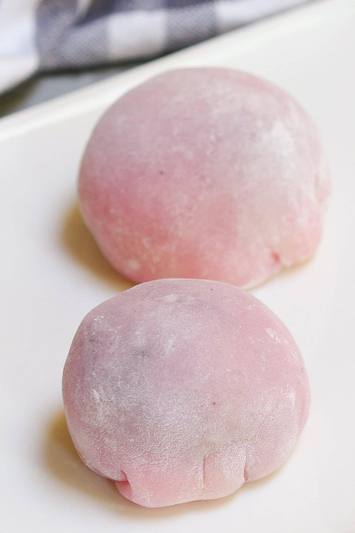Mochi 桌布 壁紙 — 兩個軟粉紅麻糬糰子撒上粉末，放在白色盤子上，背景有格子布。