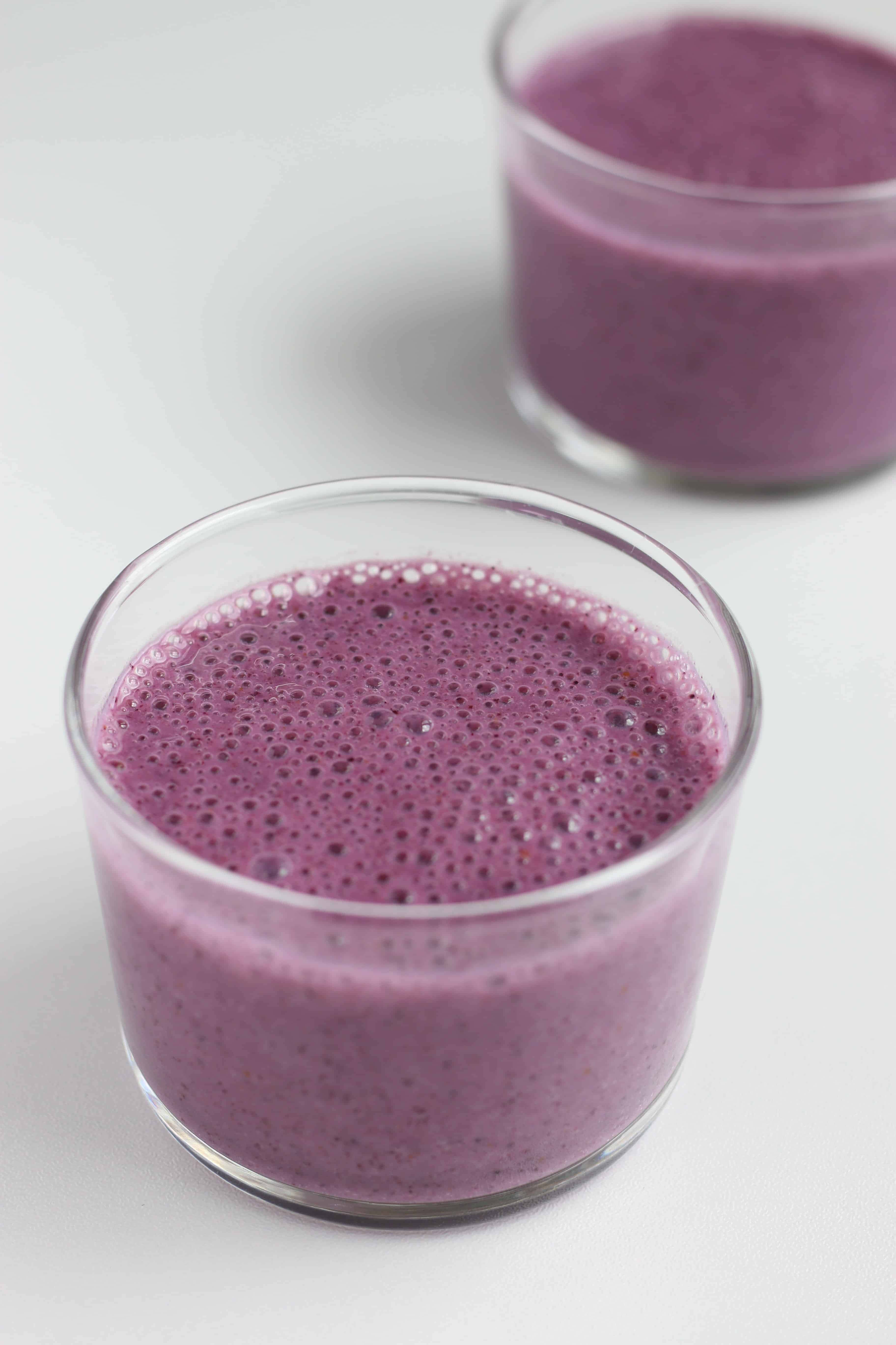 Blueberry Smoothie 桌布 壁紙 — 兩個透明玻璃杯裝滿鮮豔的紫色冰沙，放在明亮的白色表面上，帶有柔和陰影。