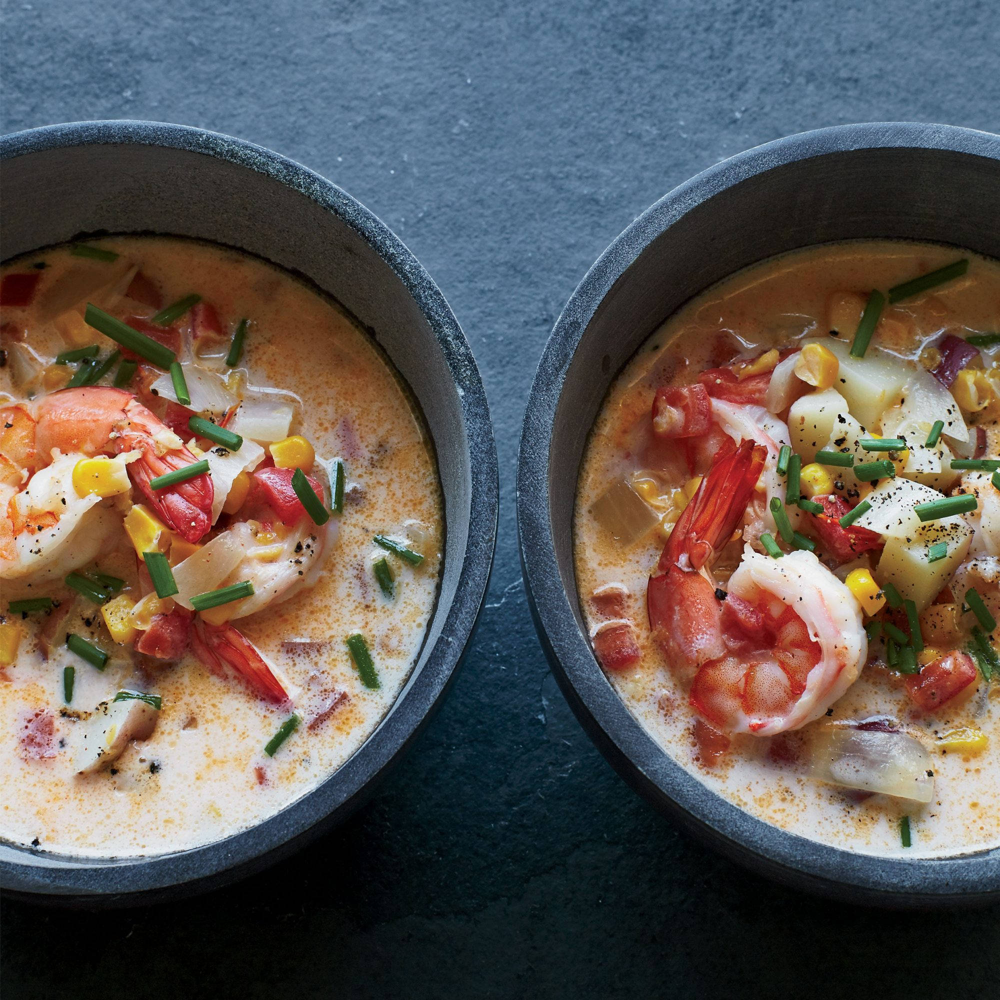 Chowder 桌布 壁紙 — 兩個鄉村風格的碗，盛載著奶油蝦仁玉米濃湯，上面撒上細香蔥和黑胡椒，放在深色石板表面上。