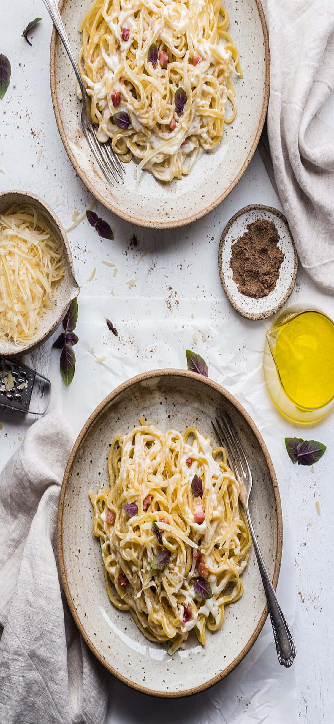 iPhone X Pasta 桌布 壁紙 — 兩個鄉村風格的陶瓷碗，盛滿奶油卡邦尼義大利麵，上面放有脆培根和新鮮羅勒，置於白色紋理表面上。