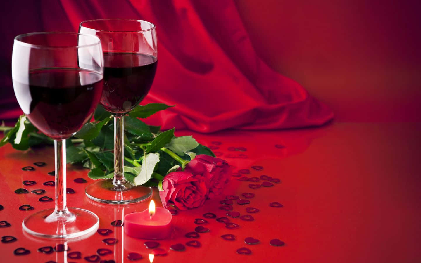 Red Wine Glass 桌布 壁紙 — 兩個酒杯、玫瑰和一支點燃的蠟燭放在一個散落著心形紙屑的紅色表面上，背景是垂墜的紅色緞面。