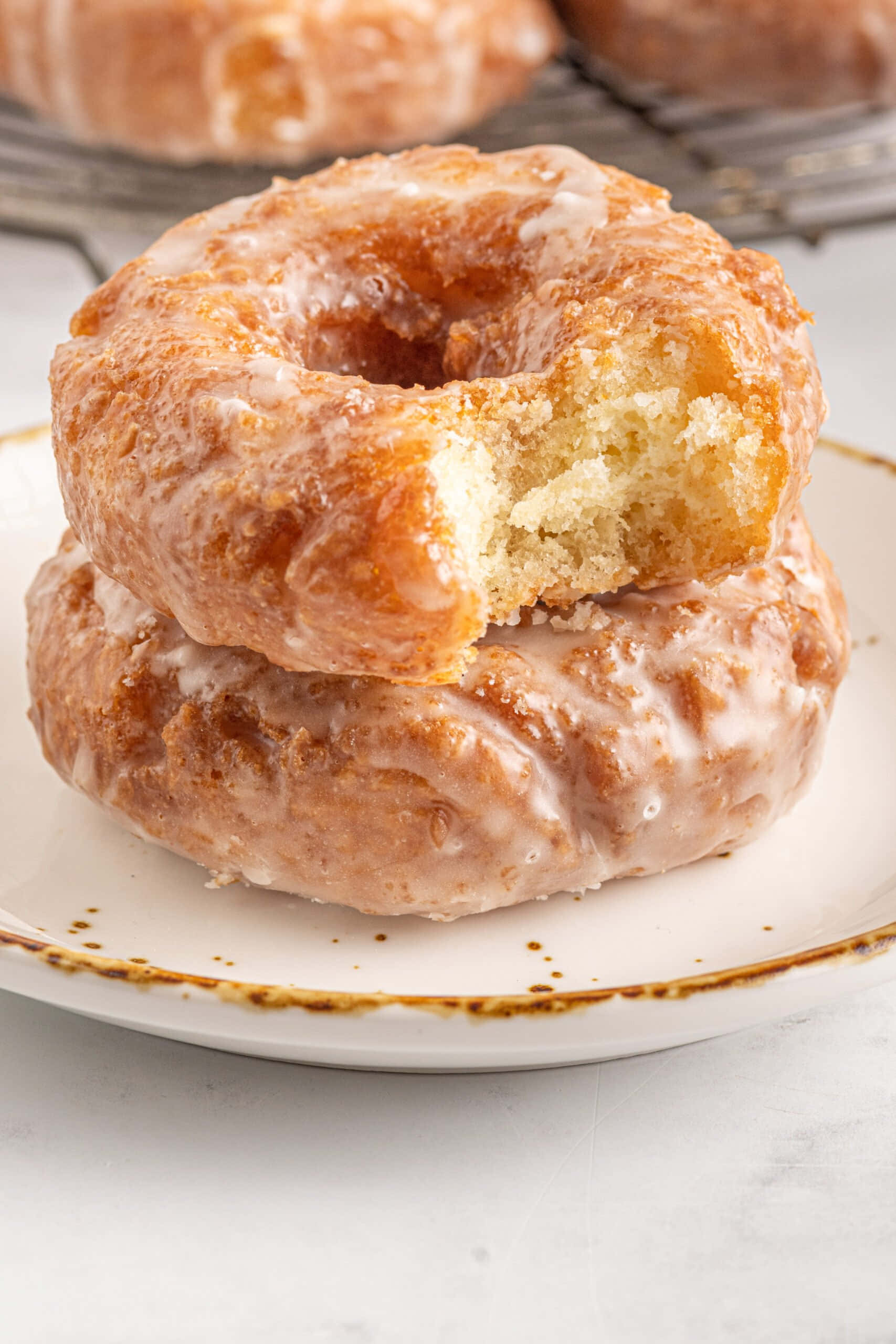 Glazed Donut 桌布 壁紙 — 兩個釉面甜甜圈疊在盤子上，其中一個被咬了一口，露出柔軟蓬鬆的內部。