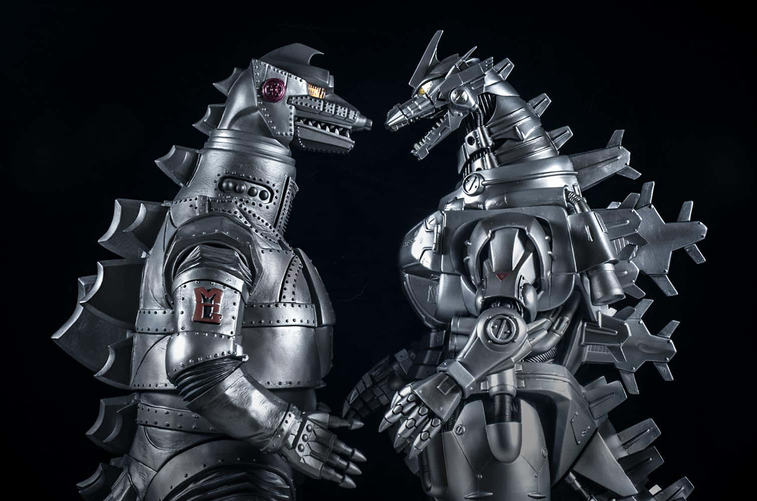 Robot Godzilla 桌布 壁紙 — 兩個金屬製的哥吉拉和王者基多拉雕像在黑色背景前進行戲劇性的攝影棚拍攝。
