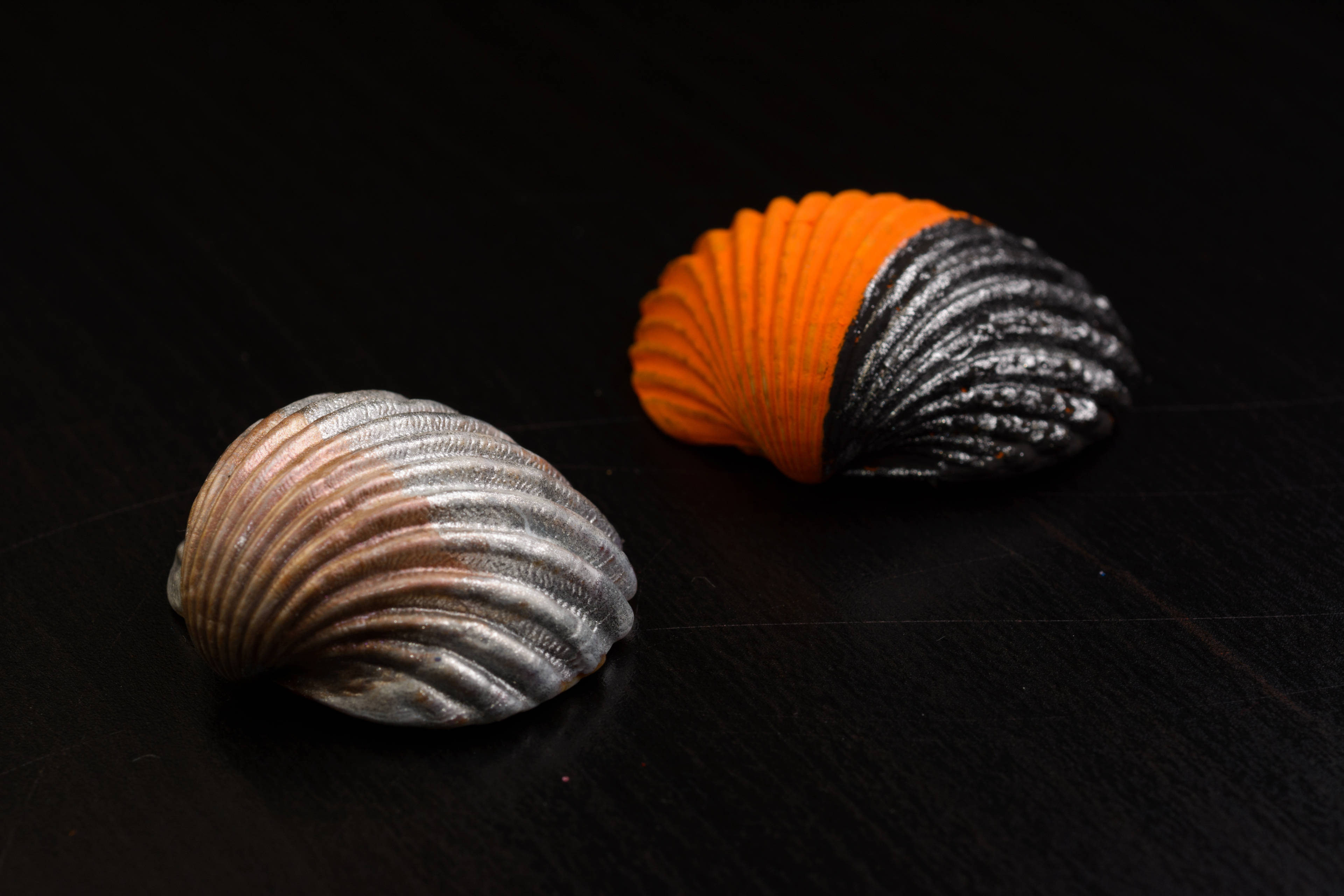 Shell 桌布 壁紙 — 兩個金屬貝殼，一個橙黑色，另一個銀棕色，放置在深色木質表面上。